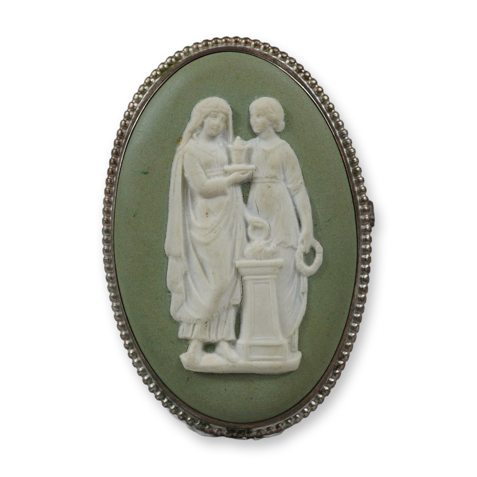 Wedgwood Sage Green Jasperware and Sterling Silver Neoclassical Oval Brooch: A vintage Wedgwood jasperware oval brooch featuring a sage green stoneware plaque with a white bas-relief neoclassical scene. The motif depicts two female figures in classical drapery; one figure stan