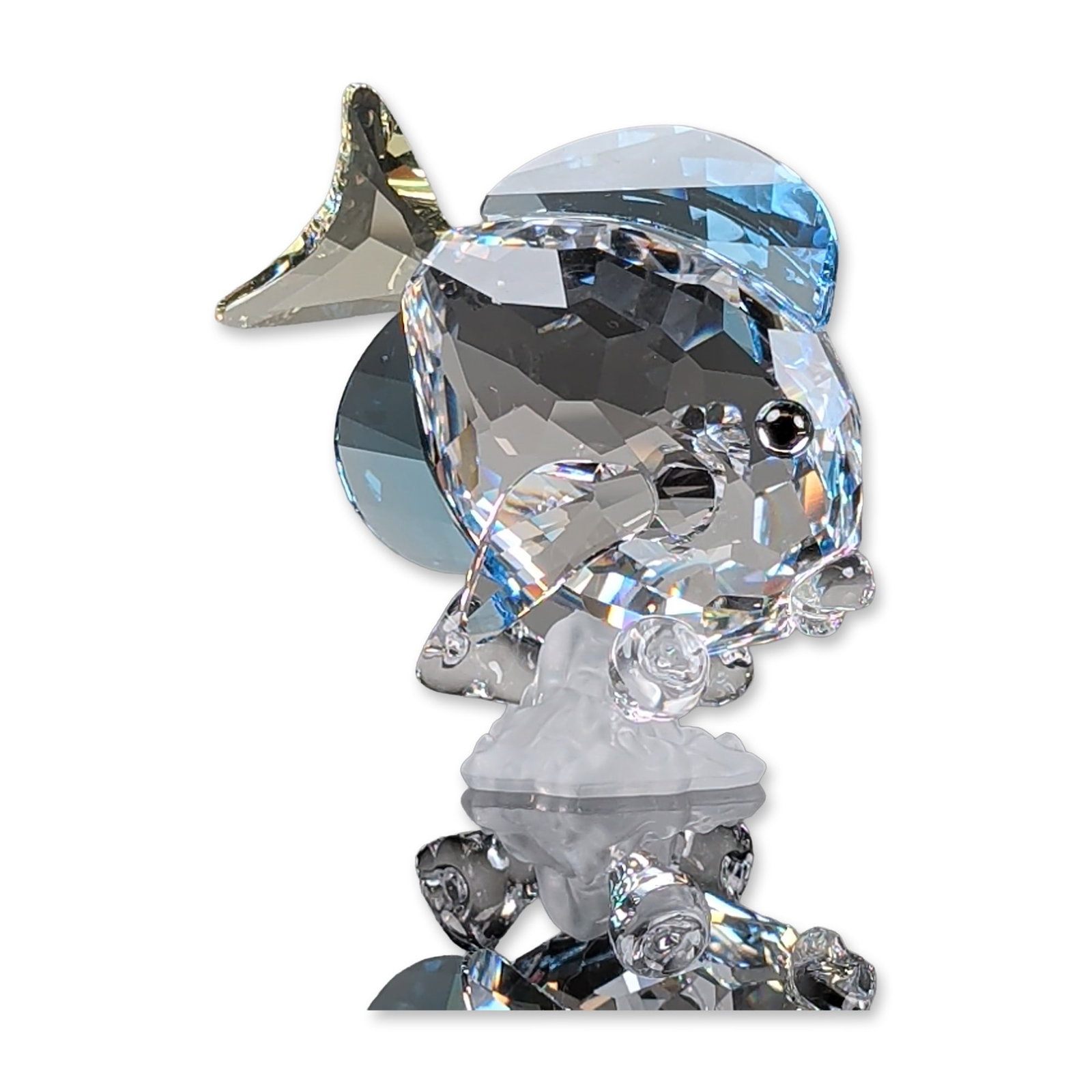 Swarovski Crystal Figurine, Blue Tang Fish: Figurine in faceted lead crystal, depicting a Blue Tang. The piece features a clear faceted crystal body accented by light blue fins and a yellow tinted tail. The fish is mounted to a frosted crystal