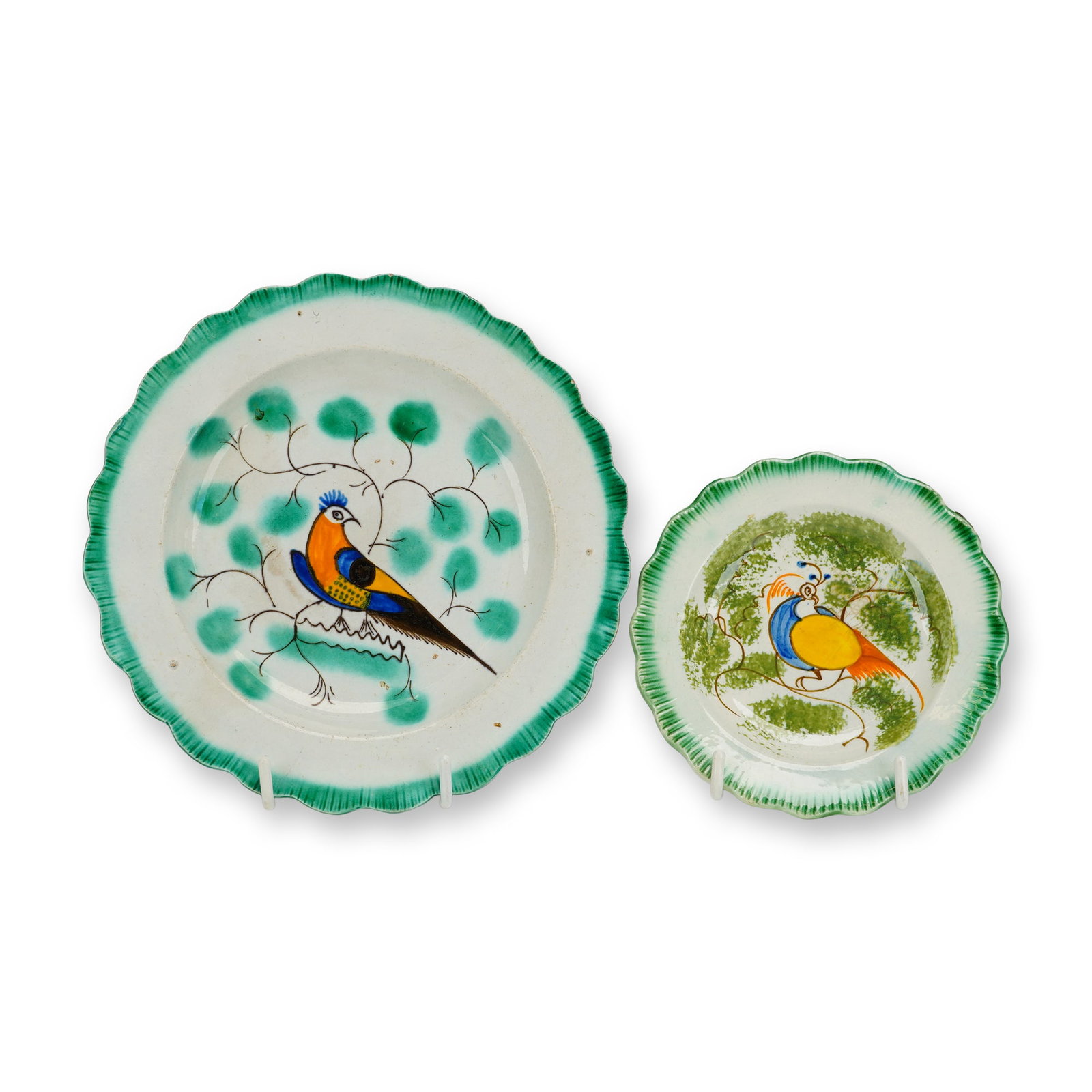 2pc English Staffordshire Pearlware Hand-Painted Peafowl Saucers: This lot features two early 19th-century English pearlware saucers. Both pieces are decorated with a hand-painted central motif of a vibrant peafowl perched on a branch, rendered in shades of orange,