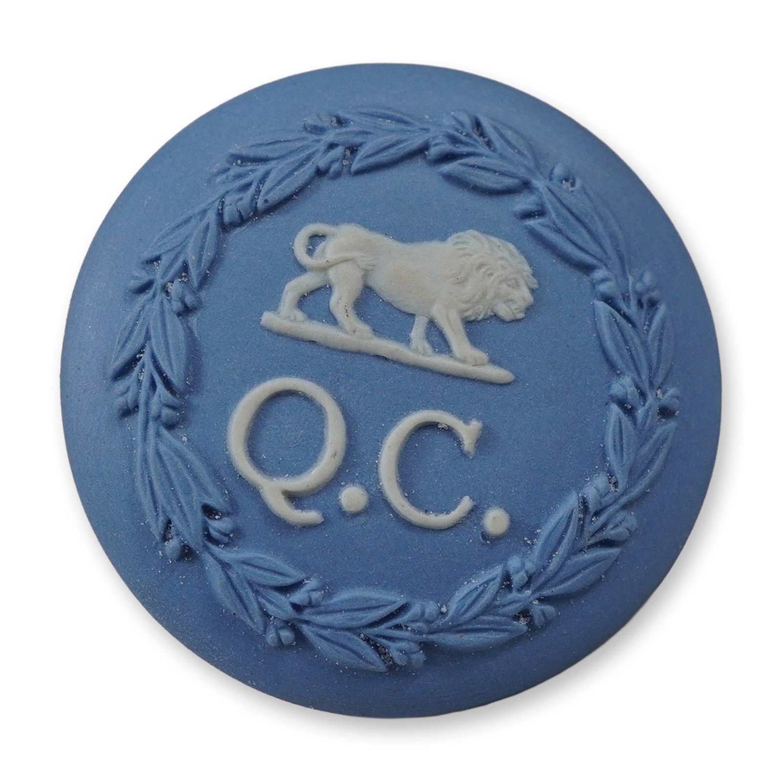 Wedgwood Blue Jasperware Pin with Lion Passant and Q.C. Motif: A circular Wedgwood jasperware pin featuring a light blue matte ground with applied white sprigged bas-relief decoration. The central motif depicts a lion passant standing above the initials Q.C.