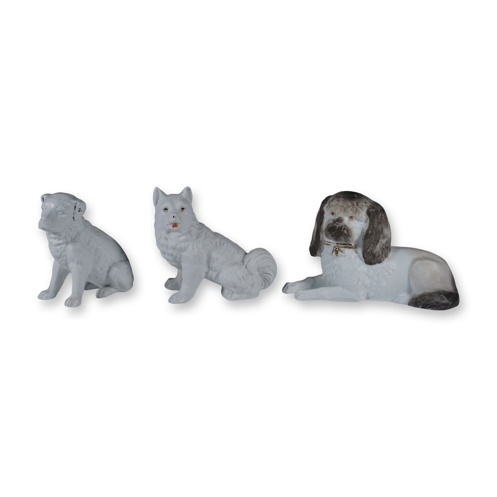 3pc Seated and Reclining Porcelain Dog Figurines: A set of three porcelain dog figurines, each uniquely crafted with fine detailing and hand-painted accents. The set includes a seated dog with black and gold highlights, a fluffy-tailed canine with su