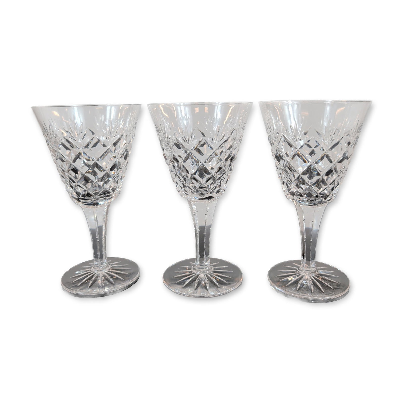 Trio of Crystal Goblets: Three goblets featuring hand-cut criss-cross diamond patterns on the lower bowl transitioning to vertical wedge cuts at the rim. The faceted stems taper to a circular foot with a sixteen-point radial 