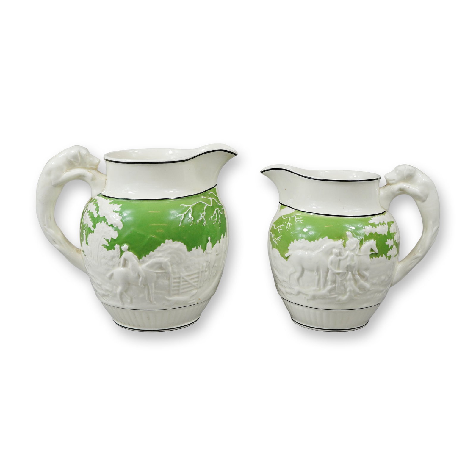 2pc Wedgwood Earthenware Hunt Pattern Pitcher Set with Hound Handles: A pair of Wedgwood molded relief earthenware pitchers of graduated sizes featuring a fox hunting motif. Each pitcher is constructed with a bulbous body, a fluted pedestal base, and a shaped pouring sp
