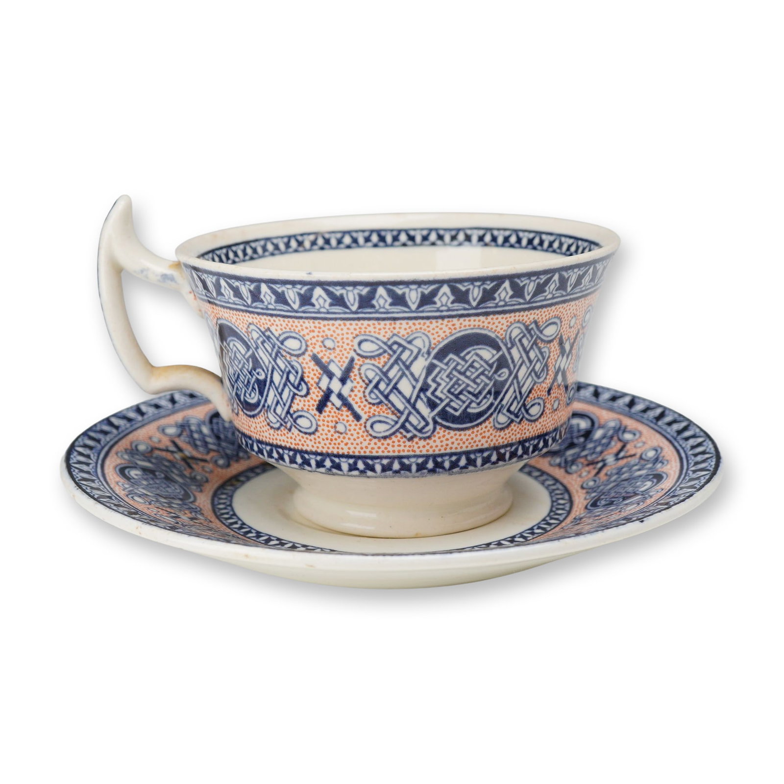 2pc Wedgwood Lindisfarne Pattern Teacup and Saucer: A teacup and matching saucer manufactured by Wedgwood in the Lindisfarne pattern. This Celtic Revival design is transfer-printed in cobalt blue against a salmon-orange stippled background. The pattern