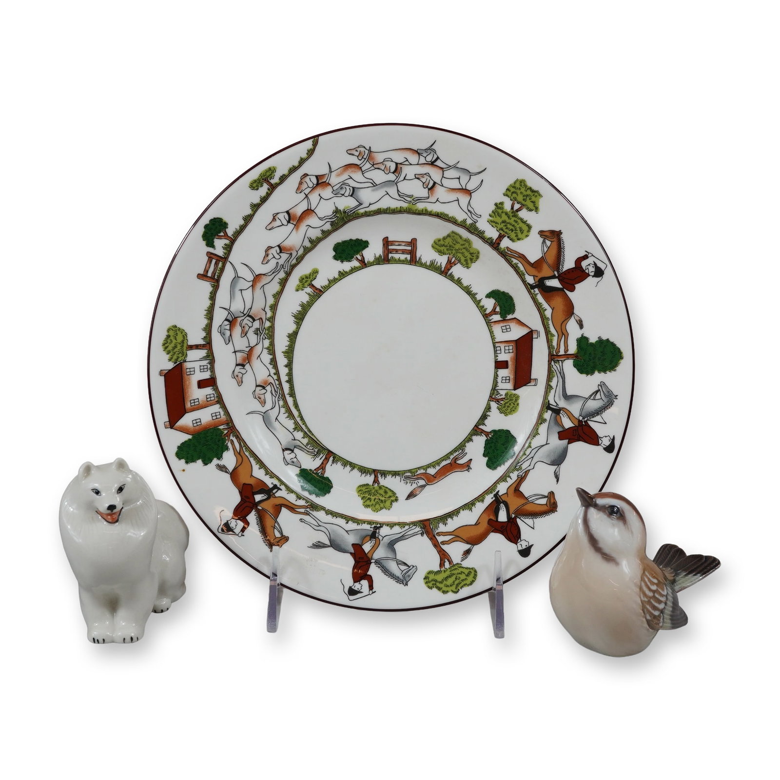 Three Porcelain Items Including a Wedgwood Plate, a Lomonosov Dog Figurine, and a Dahl Jensen Bird: This lot consists of three porcelain items: a decorative plate and two animal figurines. Each piece includes a silver-toned dealer sticker for the Rubin Collection on the base or reverse. The first it