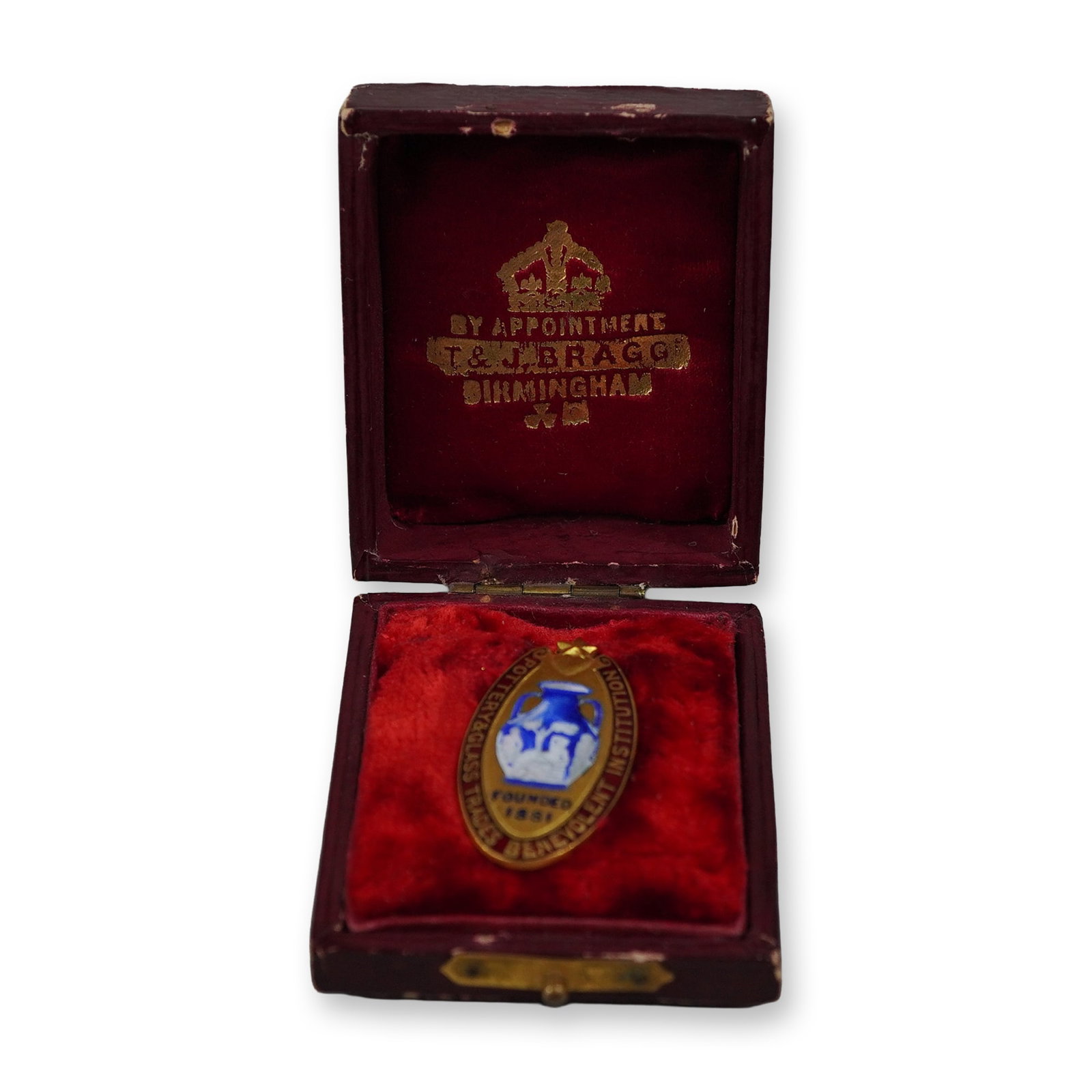 Pottery and Glass Trades Benevolent Institution Enameled Metal Pin: This lot features a vintage enameled metal pin for the Pottery and Glass Trades Benevolent Institution, an organization founded in 1881. The gold-tone oval-shaped pin features a central blue and