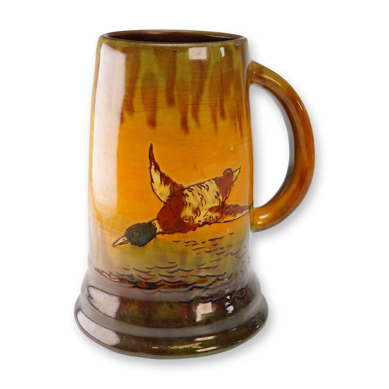 Weller Pottery Ceramic Mallard Duck Hunter Mug: This hand painted ceramic tankard features a central motif of a mallard duck in flight over water, a theme frequently explored in Weller pottery duck hunter mug series. The vessel is finished in a hig