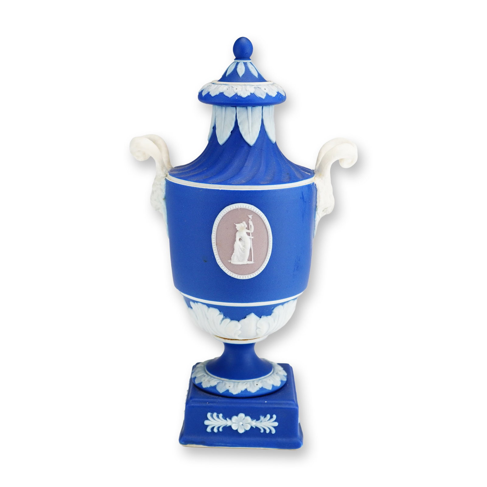 Wedgwood Blue Jasper Dip Lidded Urn with Two-Color Lilac Medallions: A Wedgwood blue jasper dip lidded urn featuring white sprigged classical relief decorations. The urn is designed with a fluted shoulder and two scrolling white handles, supported by a short pedestal f