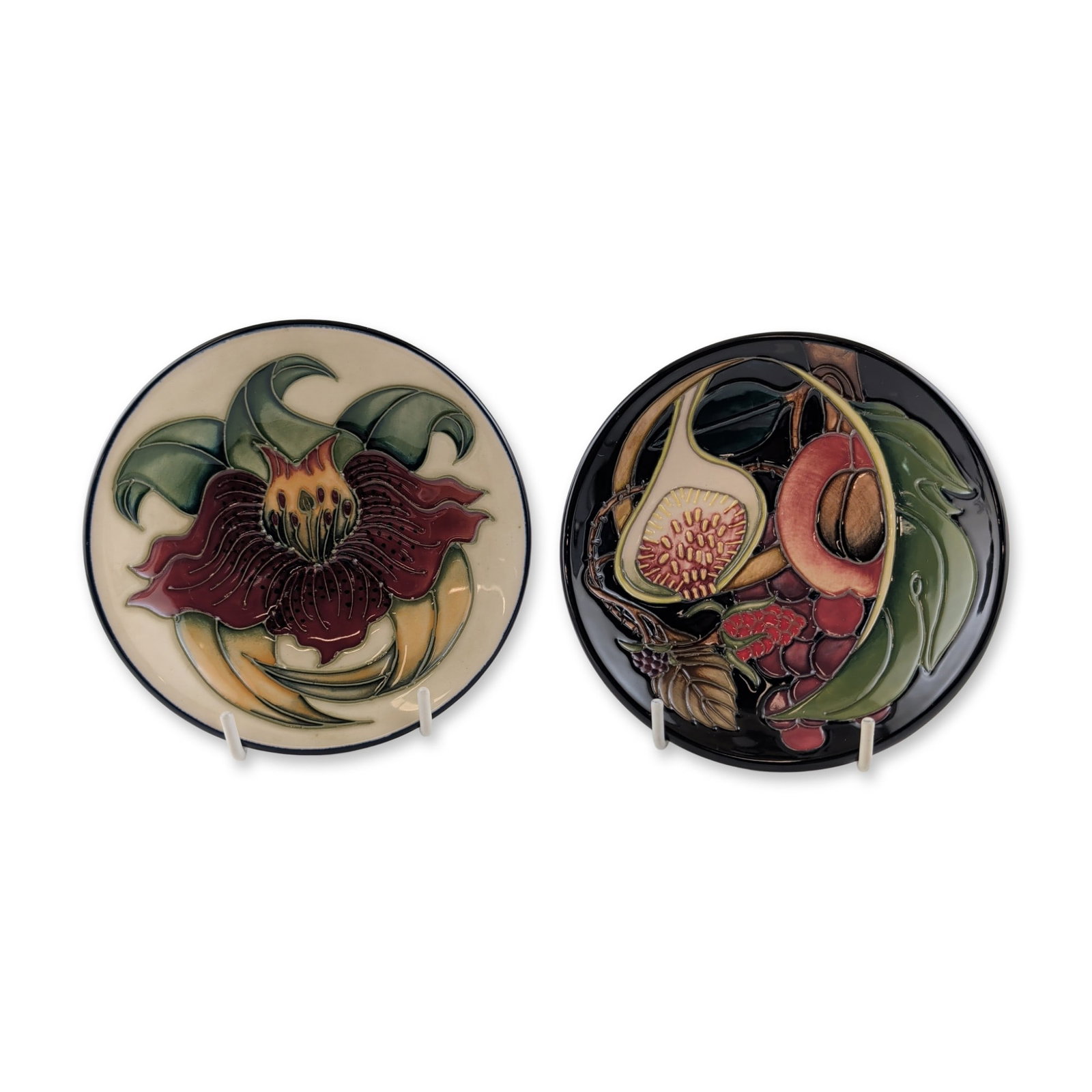 2pc Moorcroft Pottery Dishes, Queens Choice and Anna Lily: Pair of small Moorcroft earthenware dishes featuring slip-trailed tube-line decoration. One dish is decorated in the Queens Choice pattern, depicting figs, grapes, and berries on a dark navy ground. T