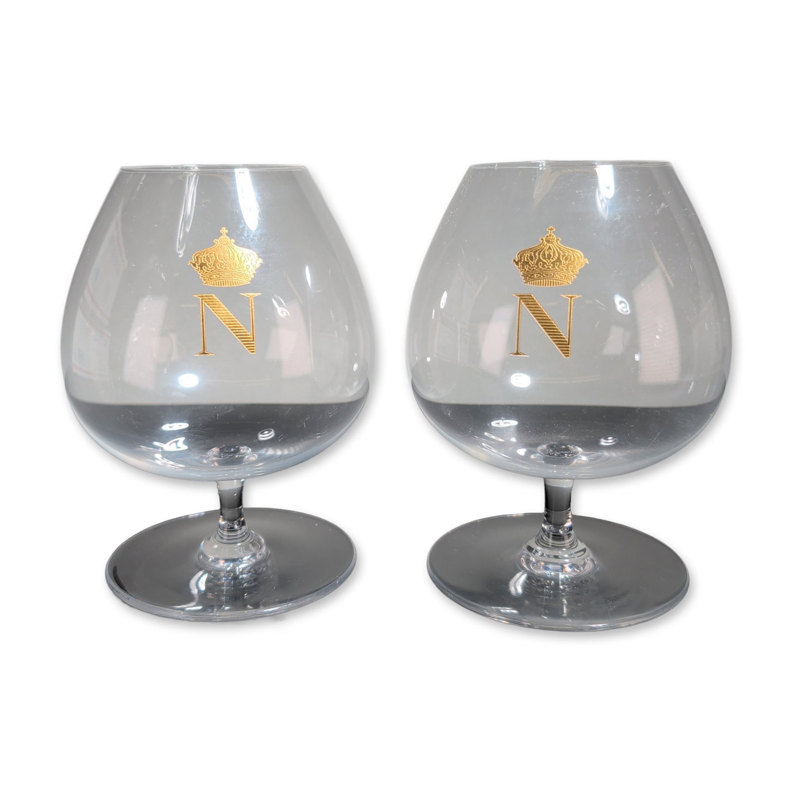 2pc Baccarat France Crystal Napoleon Brandy Snifters: Baccarat, France, pair of brandy snifters in clear lead crystal, featuring wide rounded bowls decorated with gold-gilt N monogram and Napoleonic imperial insignia. Each piece is constructed with a sho