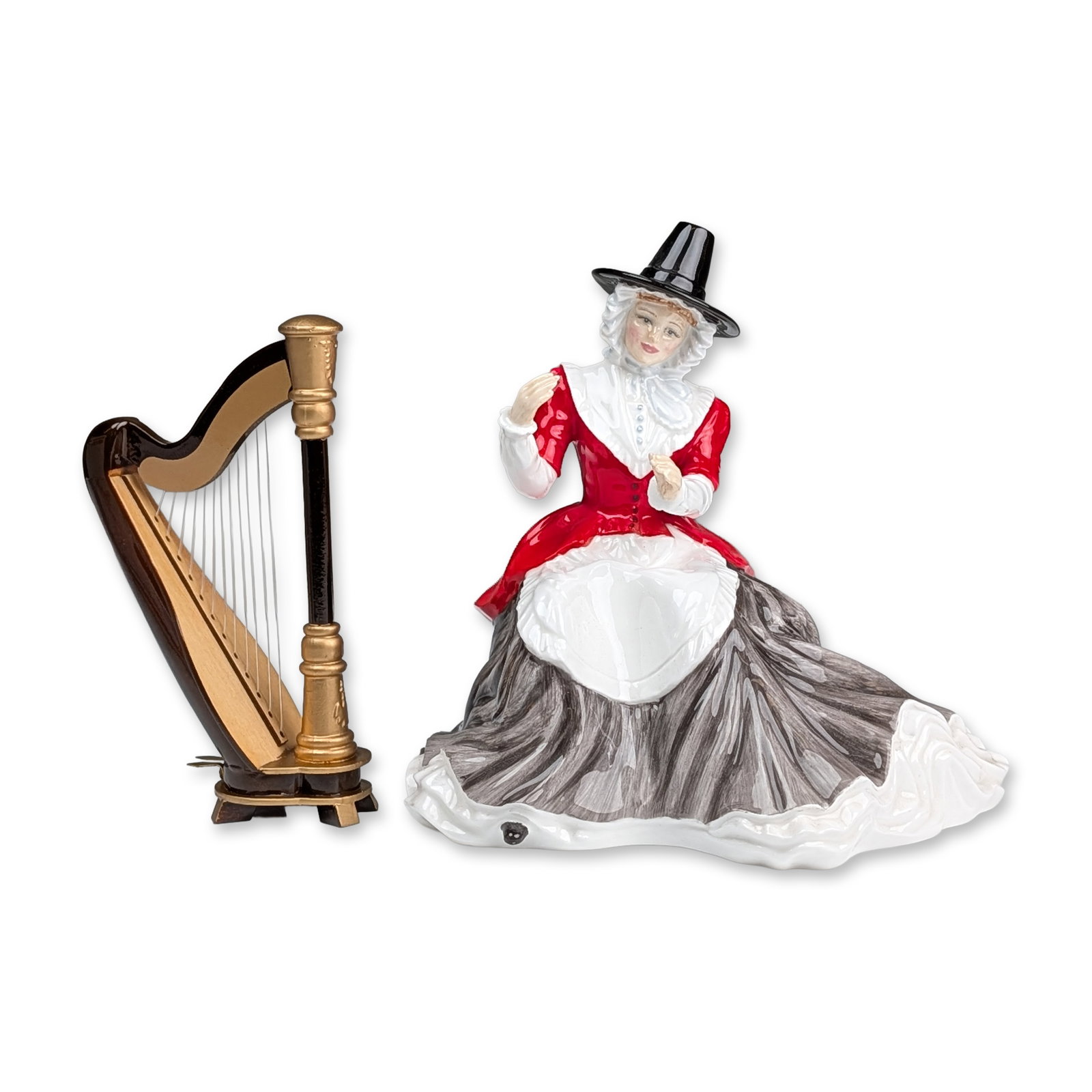 Royal Doulton by Tom Mason Prototype Tom Mason Welsh Lady Figurine with Harp: Glazed porcelain figurine of a seated woman in traditional Welsh costume, featuring a tall black hat, white ruffled bonnet, red bodice, and grey-washed skirt, accompanied by a separate miniature harp.