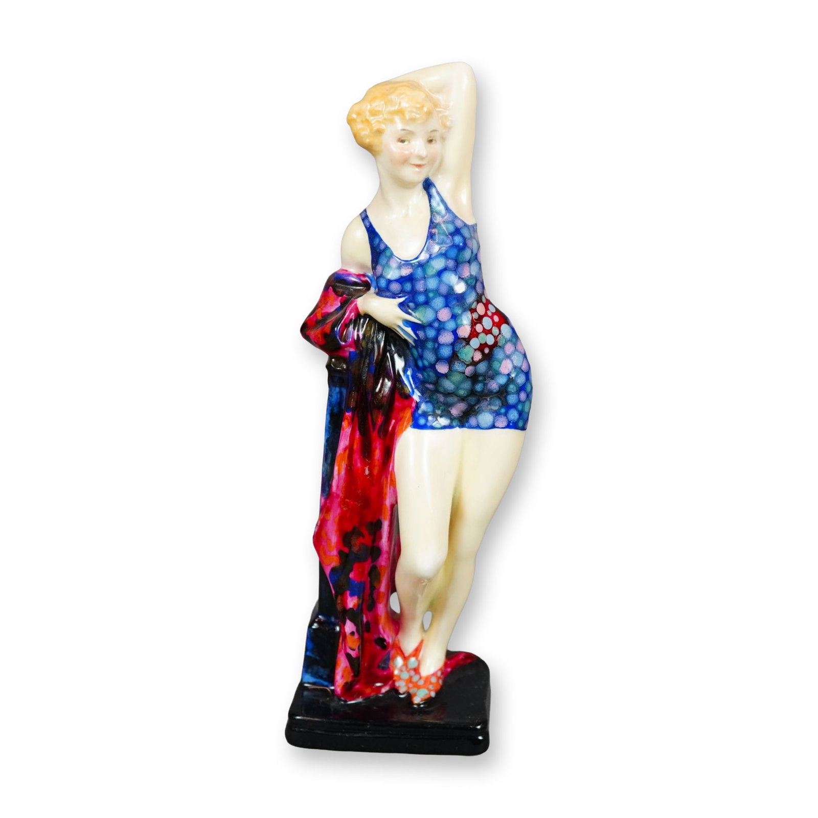 Royal Doulton Porcelain Figurine, The Swimmer: Hand painted figure of a woman in a blue swimsuit with purple and pink dots. She is shown leaning against a pedestal, holding a long dark pink and blue cloth. Royal Doulton backstamp. Artist: Alan Mas