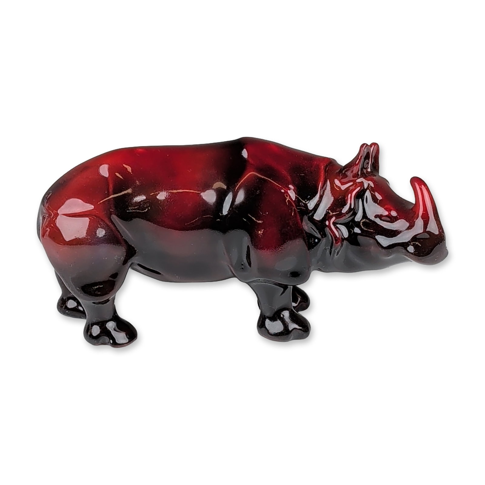 Royal Doulton Prototype Flambe Porcelain Rhinoceros Figurine: Black and red flambe-glazed figure of a rhinoceros standing on all four legs. The glaze transitions from deep red across the upper body to a rich near-black tone toward the legs and feet, creating a s