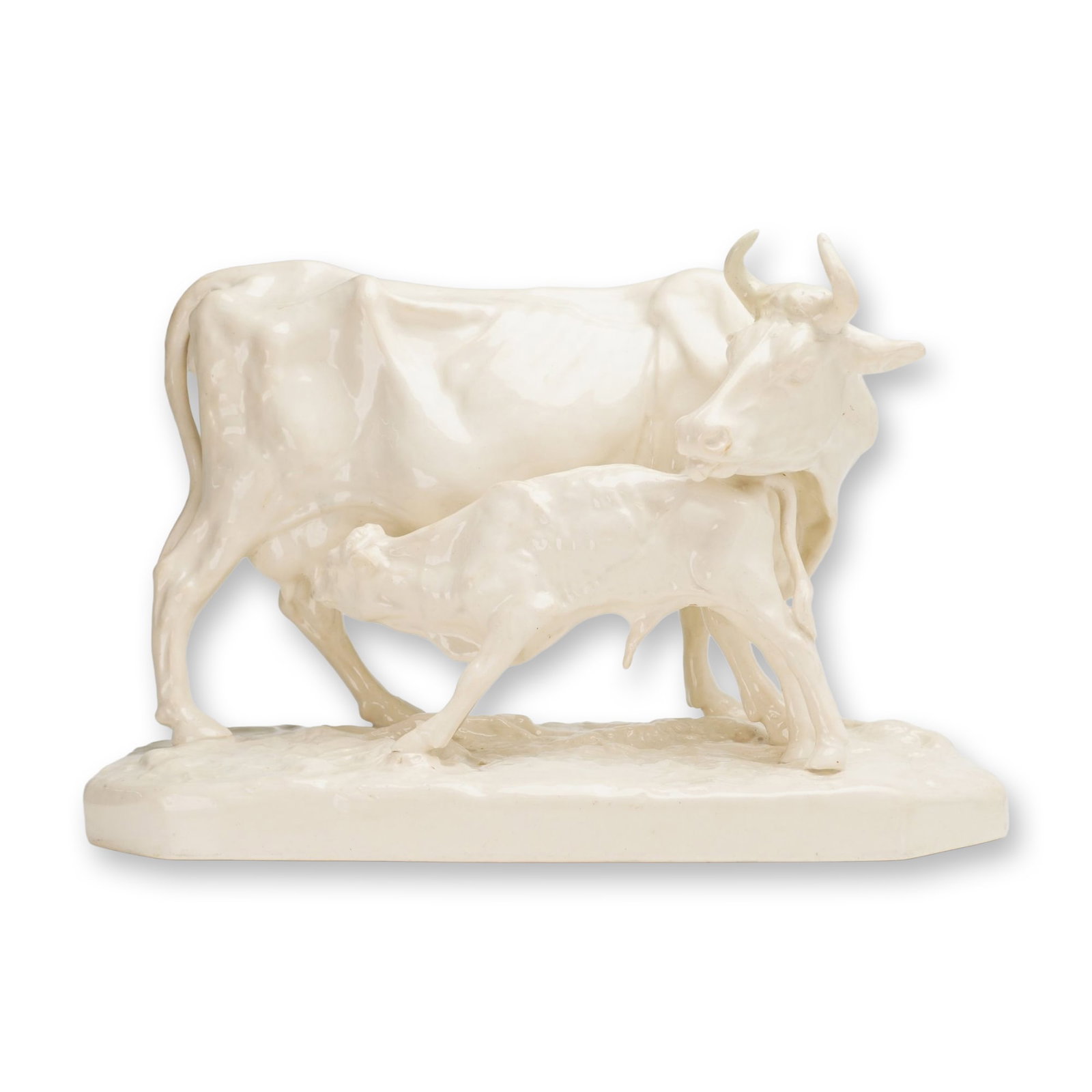 Wedgwood Glazed Creamware Figure Group of a Cow and Calf: A Wedgwood glazed earthenware figure group depicting a standing cow with a nursing calf. The figures are modeled with anatomical detail, including visible ribcages and musculature, situated on an inte