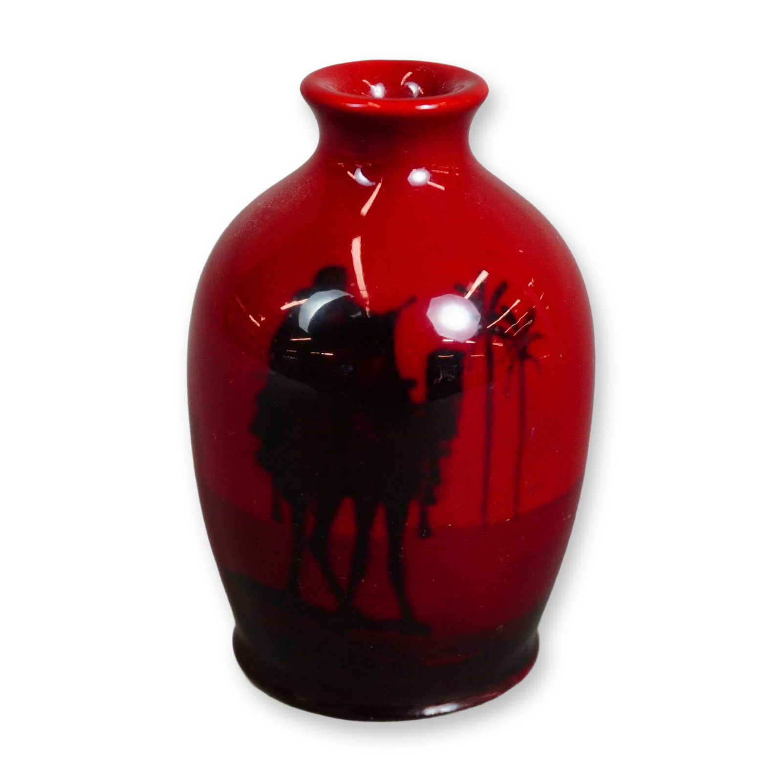 Royal Doulton Flambe Series Ware Miniature Vase, Desert Scenes: A red-flambe fired vase depicting a desert scene in black, showing a man riding a camel with palm trees in the distance. The underside bears the Royal Doulton Flambe backstamp. Dimensions: 1.75"W x 2.