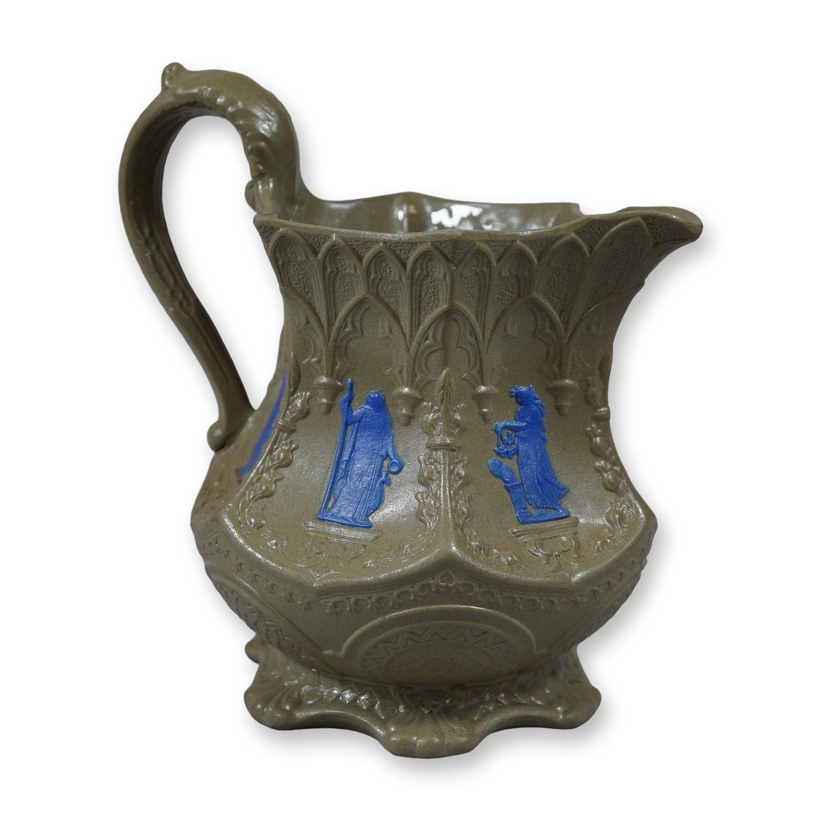 Wedgwood Mid-19th Century Smear-Glazed Stoneware Pitcher with Blue Jasperware Sprigging: This mid-19th-century stoneware pitcher, produced by the Wedgwood, exhibits a distinctive brown and blue color palette. The vessel is crafted from smear-glazed stoneware with a matte, light brown body