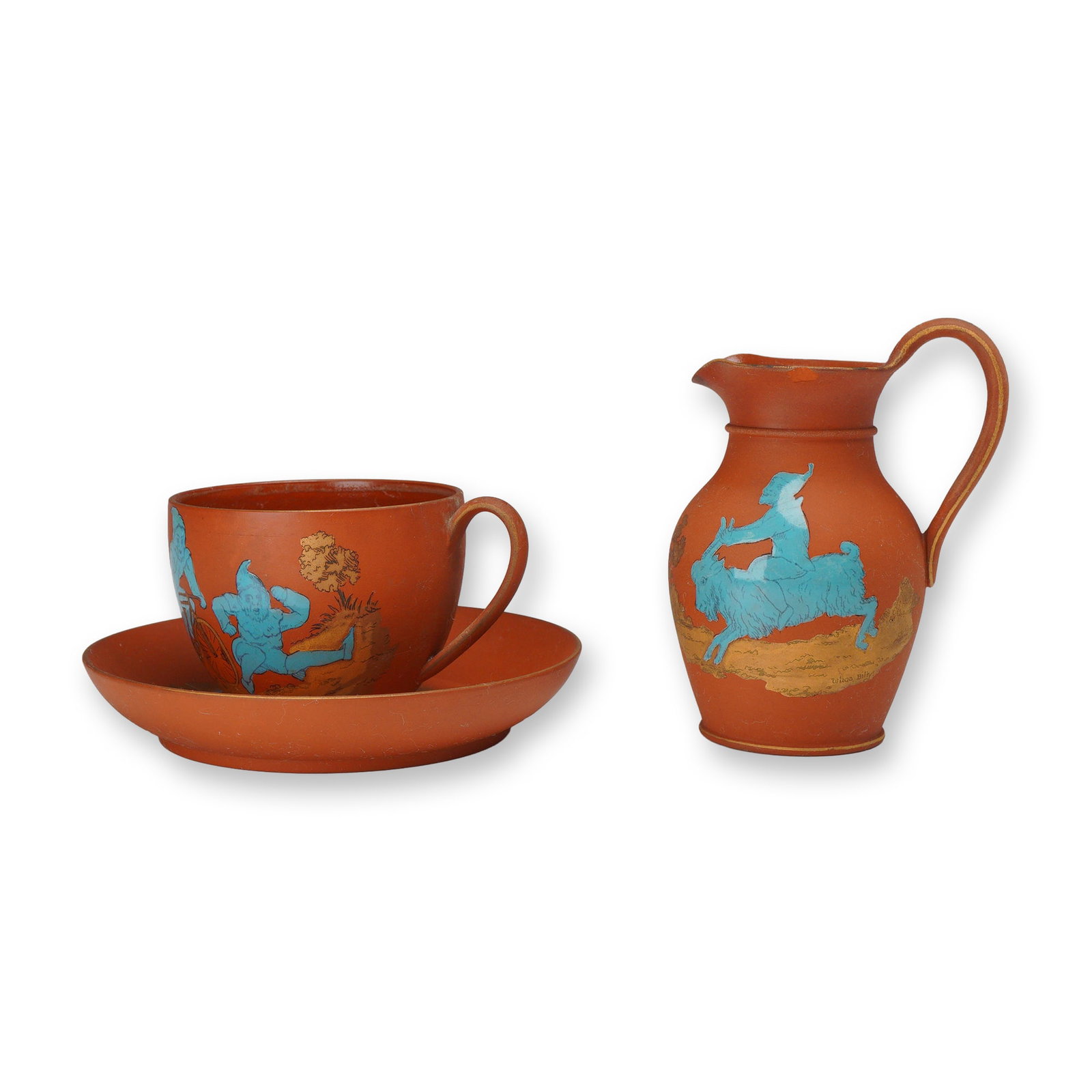Trio of Wedgwood Rosso Antico Terra Cotta Cup, Saucer & Creamer, Brownies: This three-piece ceramic set is attributed to Wedgwood and consists of a small jug, a teacup, and a saucer crafted in rosso antico terra cotta. The pieces are decorated with whimsical figures in light