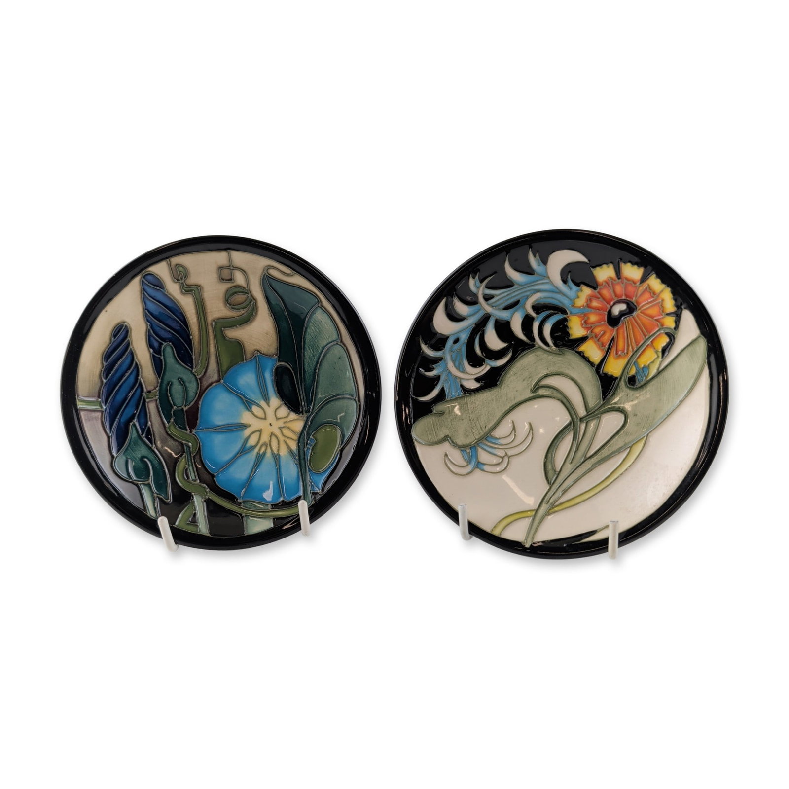 2pc Moorcroft Pottery by Emma Bossons Ceramic Floral Pin Dishes: One dish depicts the Lily Plume pattern designed by Emma Bossons for the Moorcroft Collectors Club (MCC), characterized by a stylized lily in orange and yellow with blue feathery motifs on a cream gro