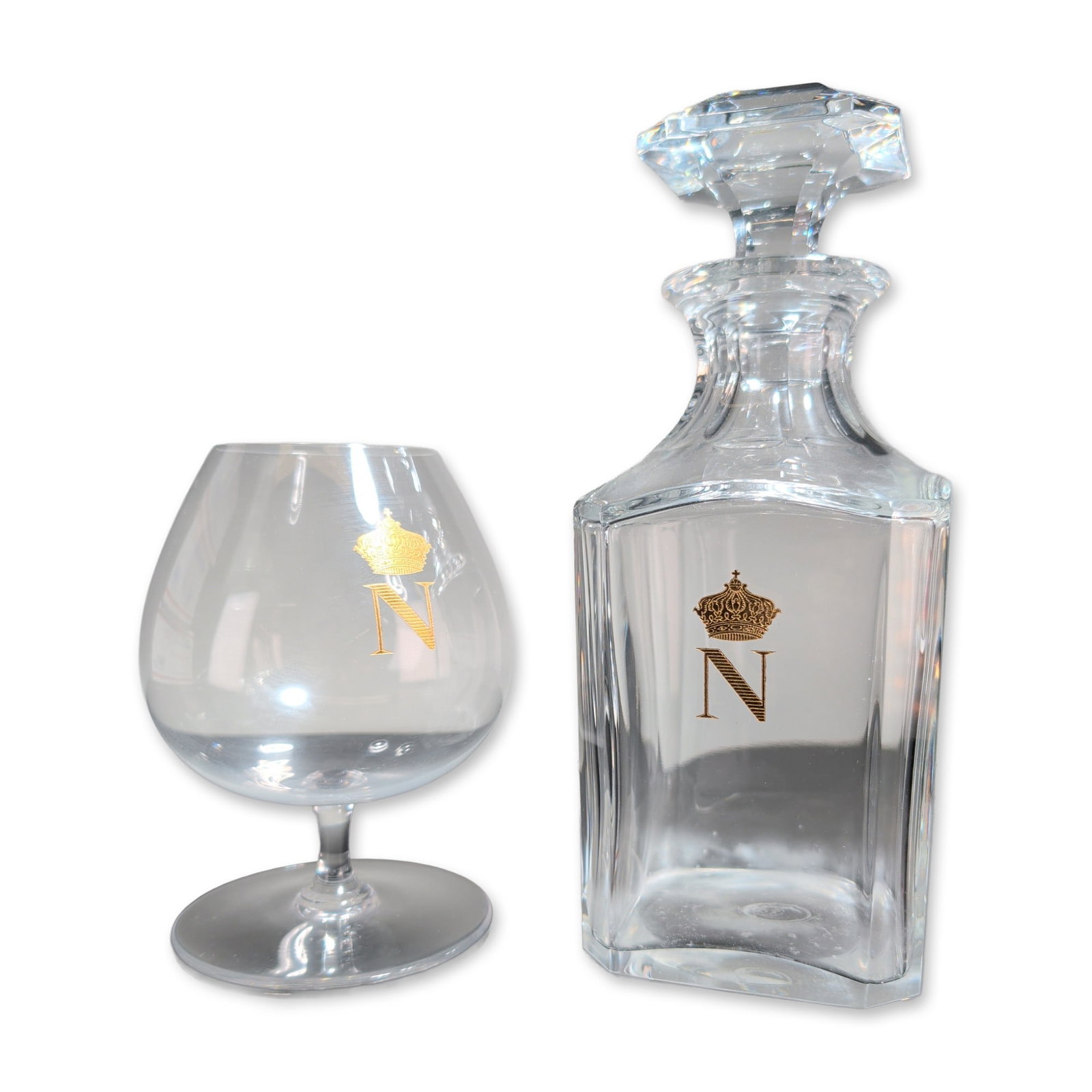 2pc Baccarat Crystal Napoleon Decanter with Stopper and Snifter: Baccarat, France, spirit decanter and matching brandy snifter in lead crystal, each featuring an applied gold gilt Imperial Napoleon N monogram beneath a crown. The decanter of square form with rounde