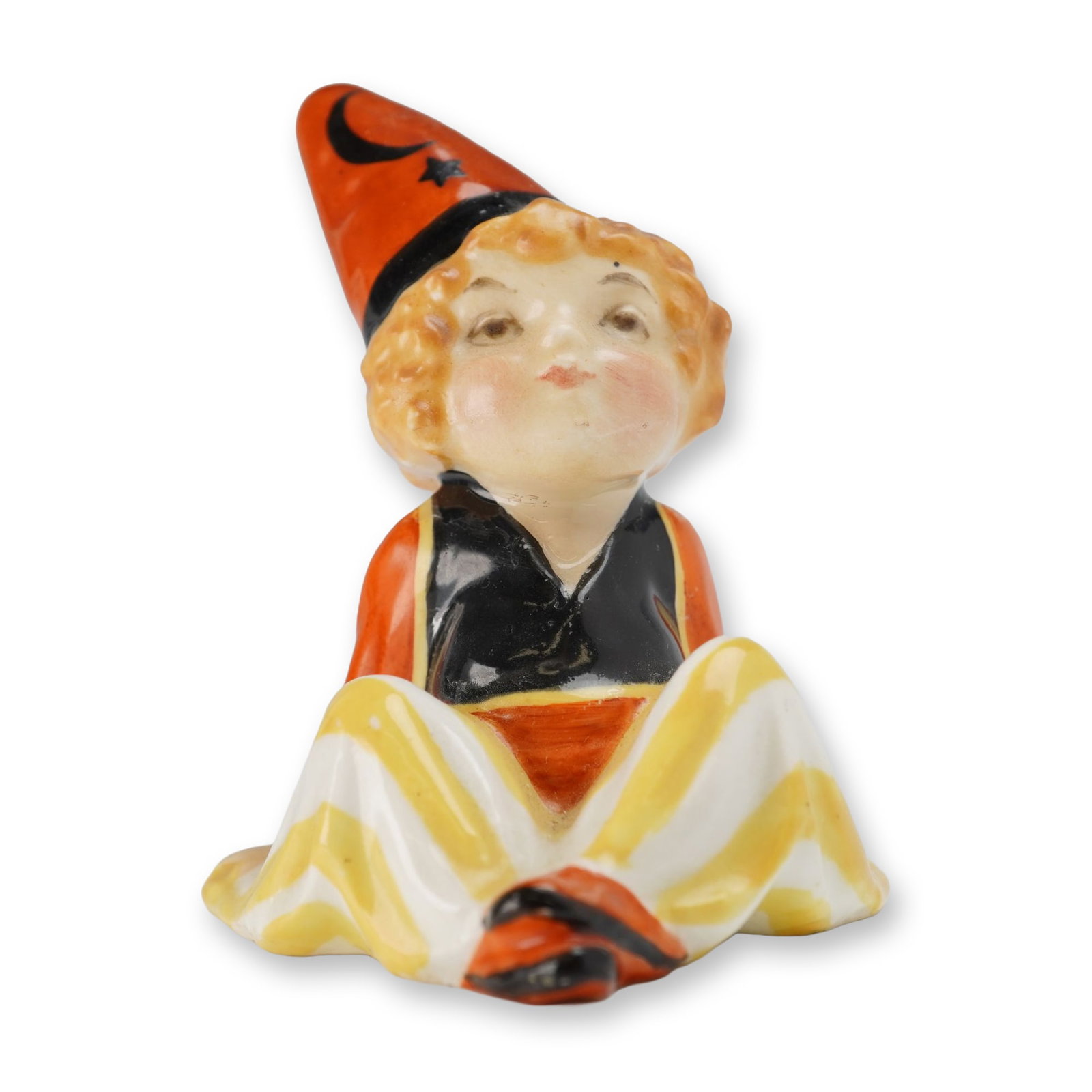 Royal Doulton Porcelain Figurine, Cassim HN1232: Designed by Leslie Harradine. The glazed ceramic figure depicts a seated character with curly hair looking upward, wearing a pointed orange hat adorned with a black crescent moon and star, a black ves