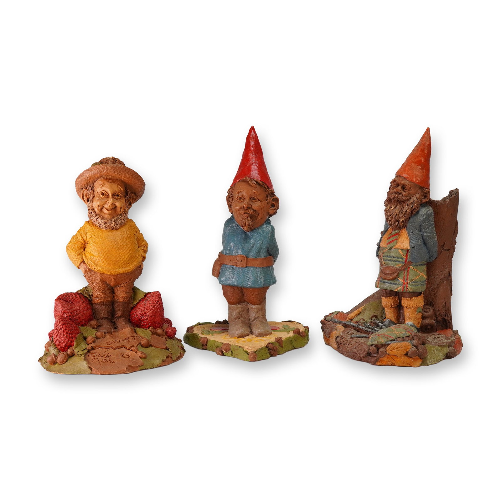 Three Tom Clark Cairn Studio Gnome Figurines: A trio of painted resin gnome figurines designed by artist Tom Clark for Cairn Studio. This collection includes the 1984 Shorty figure, featuring a strawberry guy in a yellow sweater and wide-brimmed 