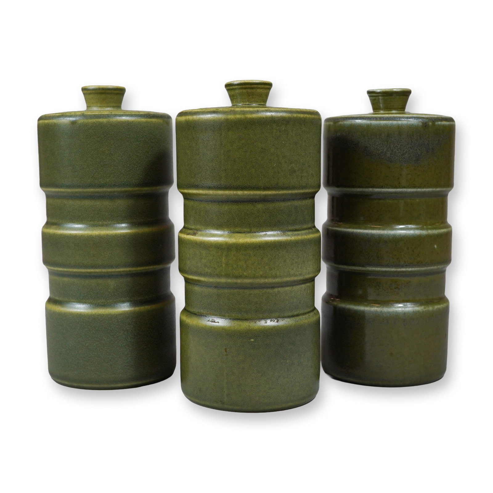 Three Keith Murray for Wedgwood Matte Green Glazed Canisters: A trio of cylindrical earthenware canisters designed by Keith Murray for Wedgwood. Each canister is finished in a uniform matte olive green glaze and features three prominent horizontal bands. The can
