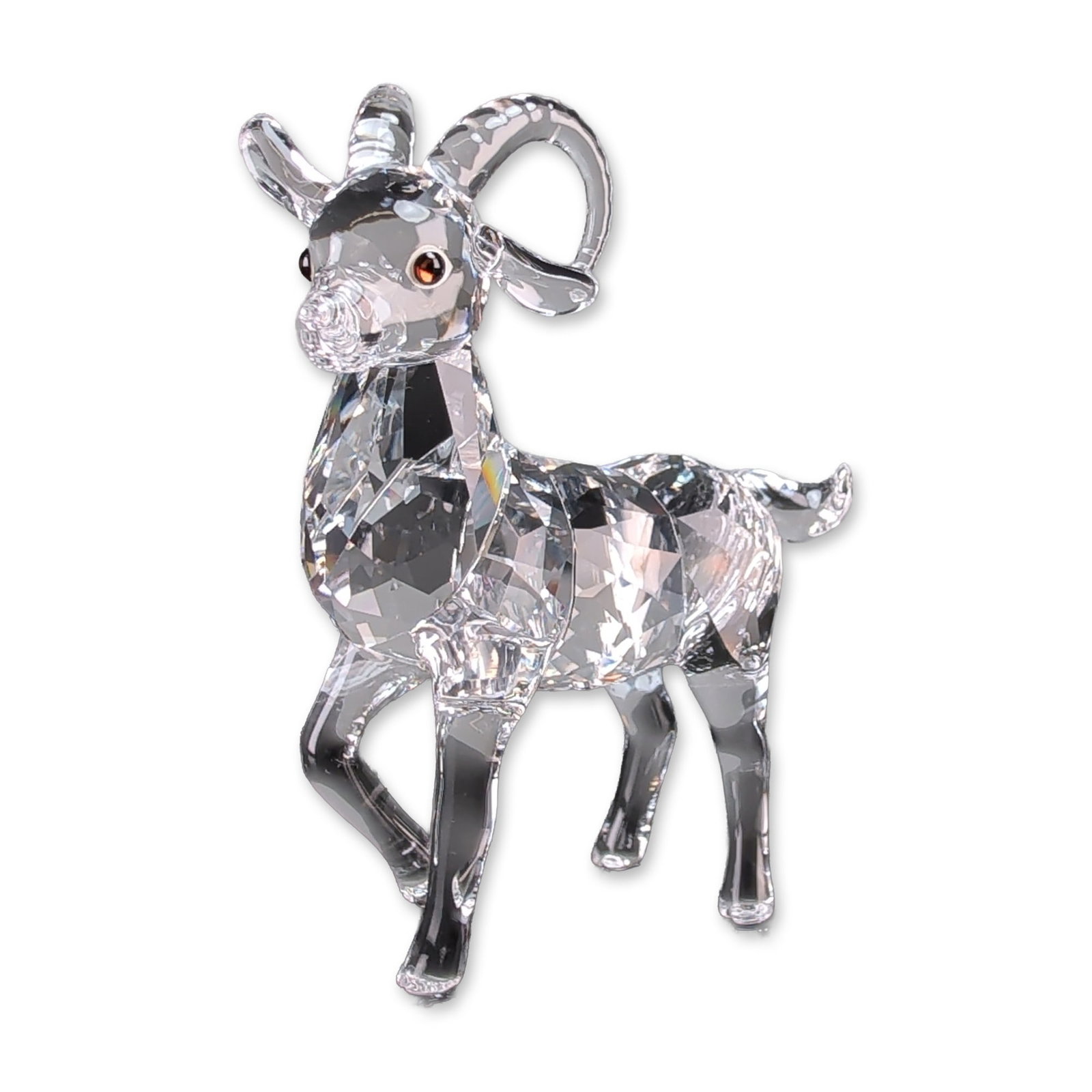 Swarovski Clear Crystal Ibex Figurine: Swarovski figurine in faceted clear lead crystal, depicting a standing ibex with swept-back curved horns and small inset amber-colored eyes. The piece is constructed with precision-cut geometric facet