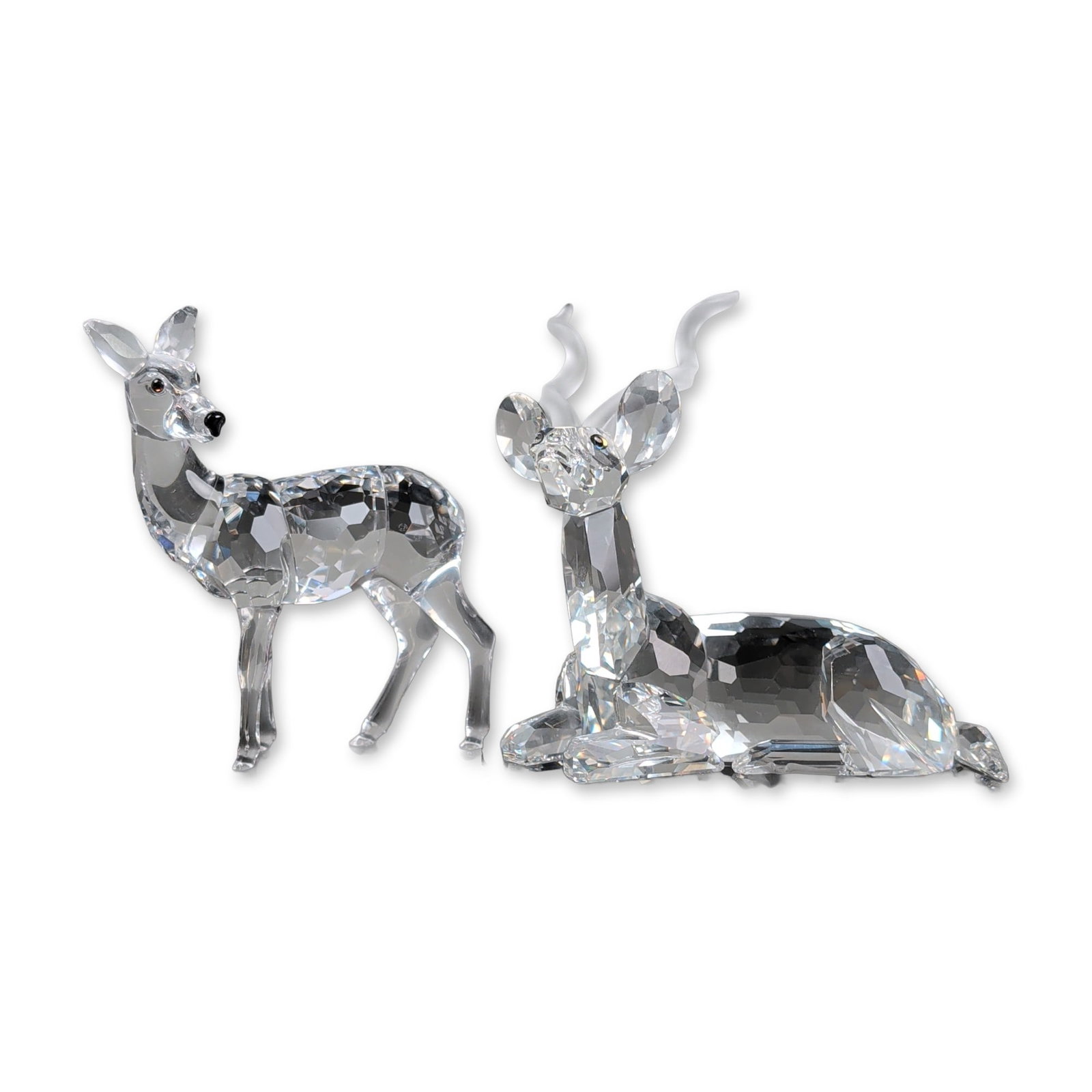 2pc Swarovski Crystal SCS Inspiration Africa Figurines, Kudu and Doe: Two faceted clear lead crystal kudu and doe figurines, including a seated male with frosted spiraled horns and a standing doe. Both figures are accented with small black crystal eyes. Seated figure ma