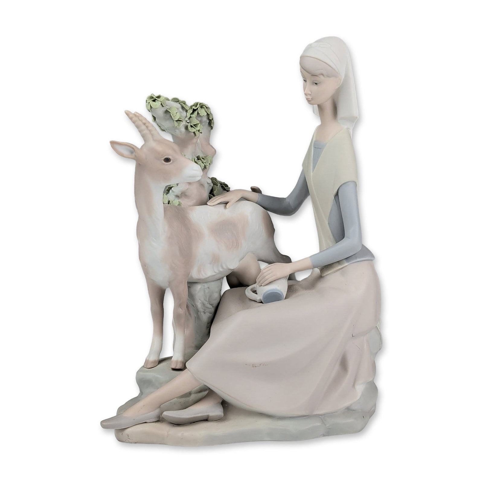 Lladro Matte Porcelain Figurine, Girl with Goat 01004570: The composition features a seated young woman in traditional dress, including a headscarf, tunic, and long skirt, positioned beside a goat and a stylized tree with applied ceramic foliage. The figure 