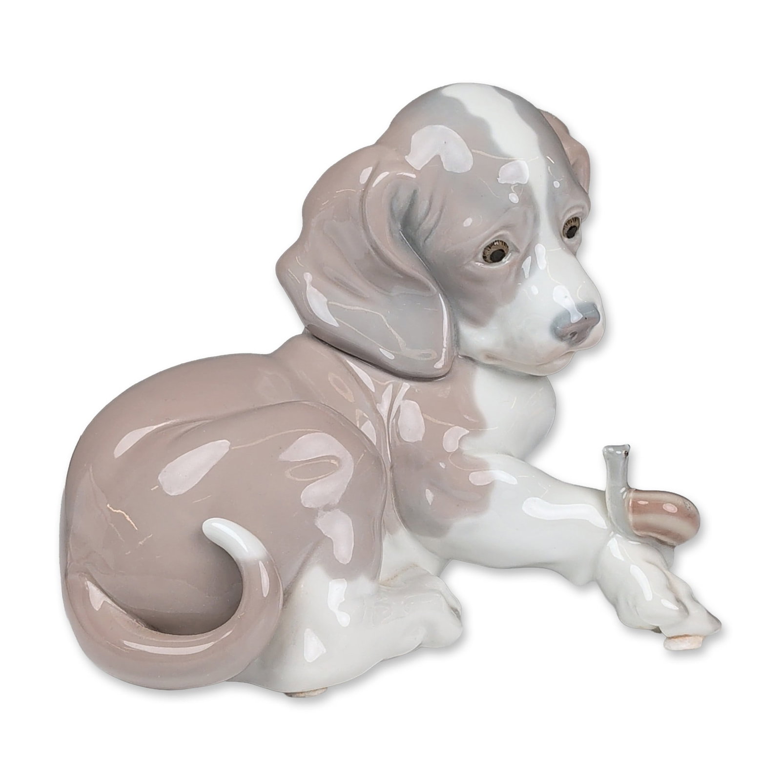 Lladro Glazed Porcelain Figurine, Dog and Snail 01001139: Figurine depicts a sitting puppy with a small snail on his front paw. The piece is finished in a high-gloss glaze using a palette of soft gray, tan, and white tones. Base bears the blue Lladro backsta