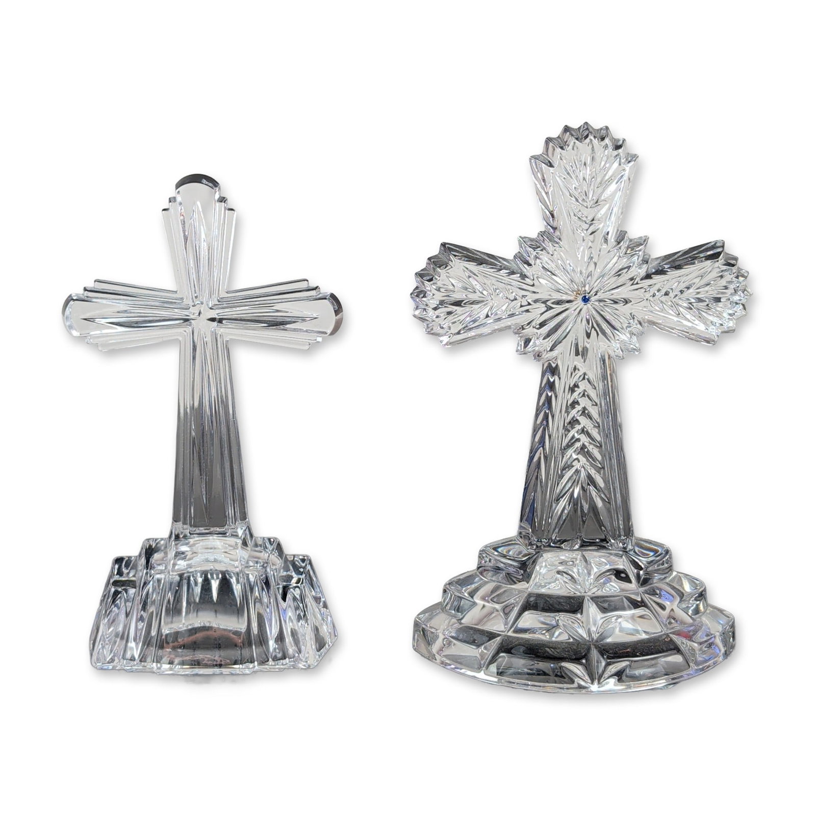 2pc Lenox and Waterford Lead Crystal Standing Crosses: Lead crystal standing crosses in two distinct designs. The larger example features a central starburst motif with a blue crystal inset, a stem with chevron-cut accents, and a domed circular base with 