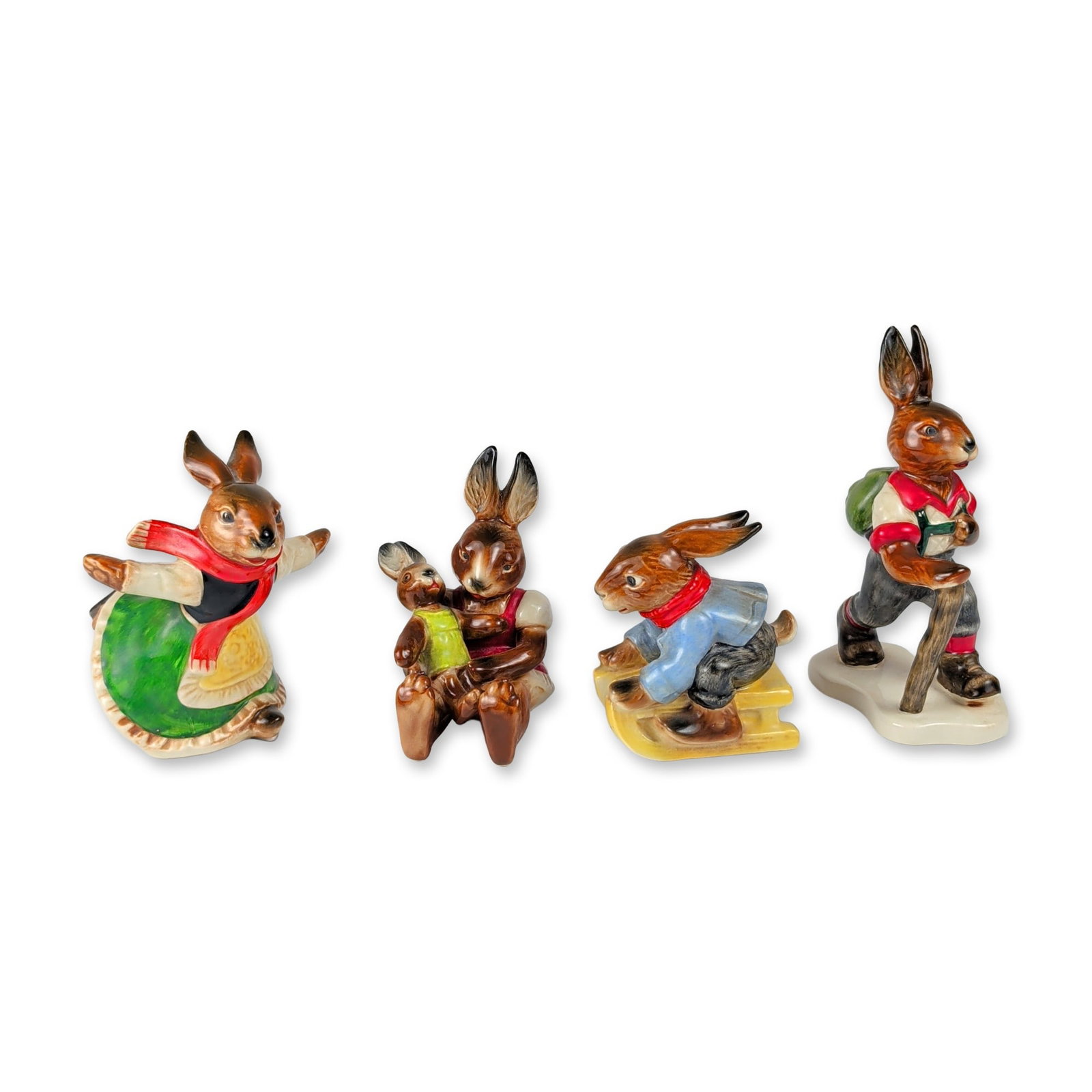 4pc Goebel West German Rabbit Figurines Collection: Goebel, West Germany. Collection of glazed ceramic figurines depicting anthropomorphic rabbits in various activities, including a hiker with a walking stick and backpack, a figure on a yellow sled, a 