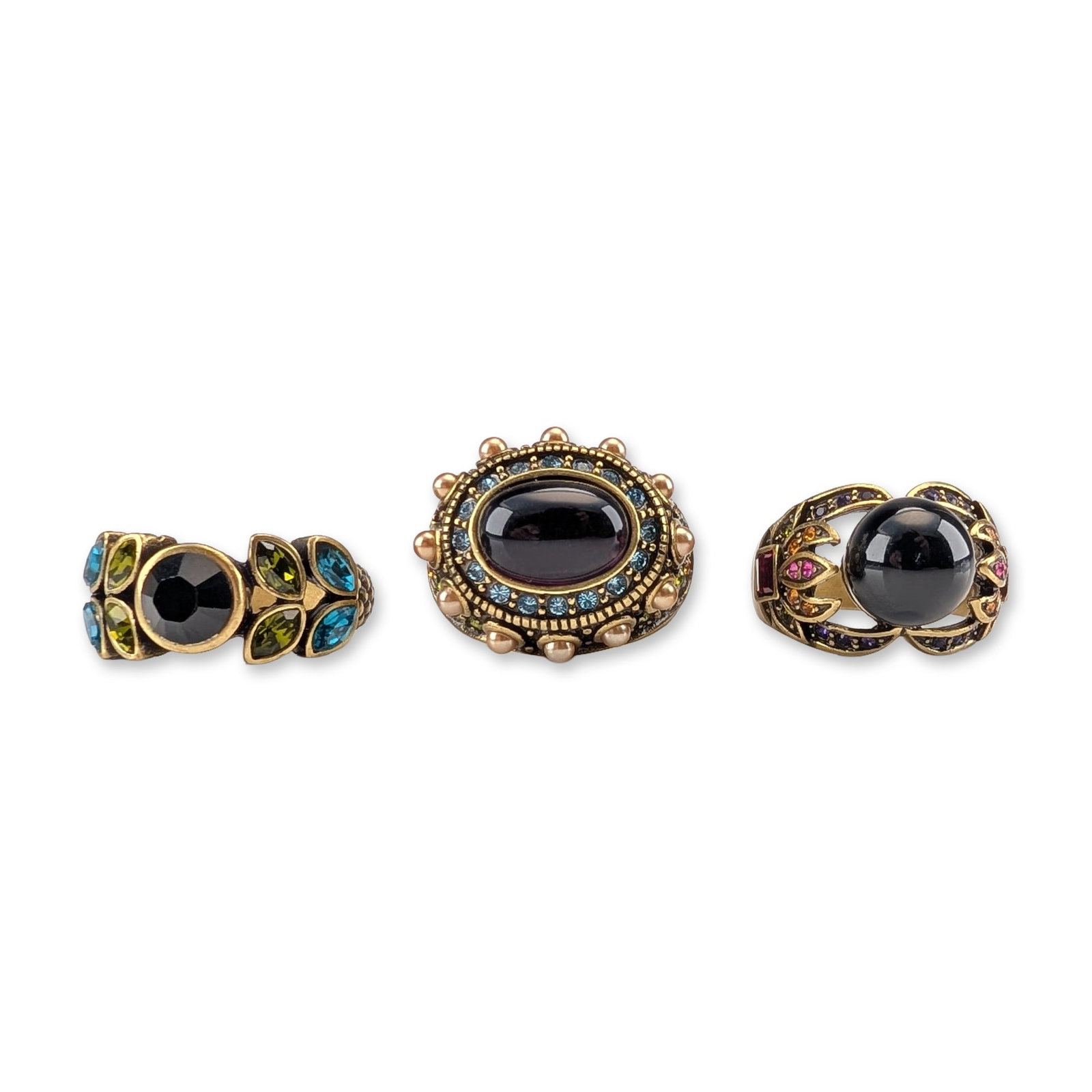 3pc Heidi Daus Bronze Tone and Crystal Cocktail Rings: Trio of cocktail rings in antiqued bronze-tone base metal, featuring black glass cabochons, a purple cabochon, and multi-colored faceted crystal embellishments. The collection includes a leaf-motif ri