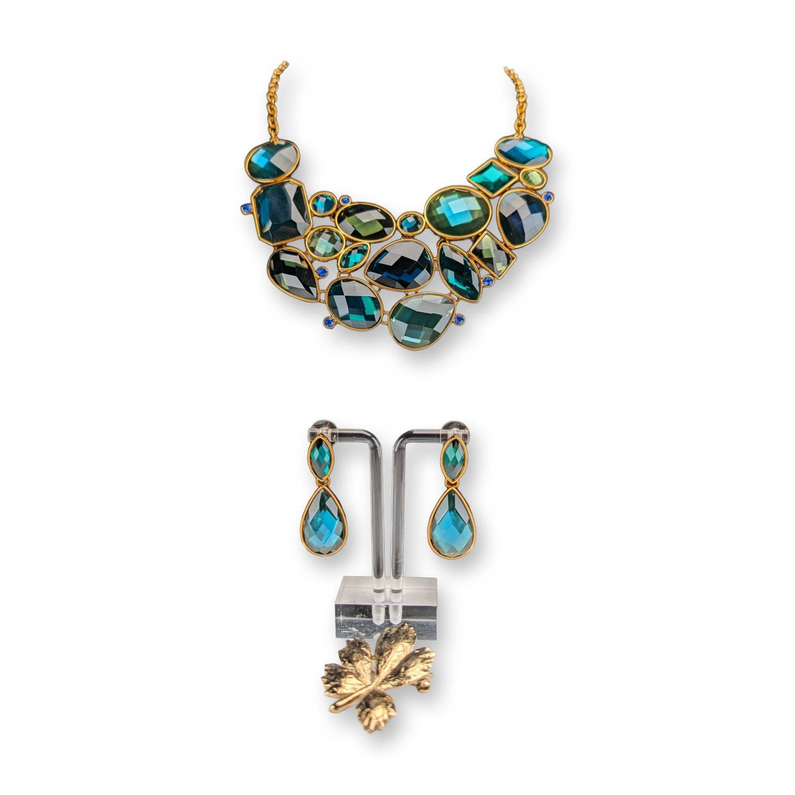 4pc Joan Rivers Classics Collection Jewelry Suite and Brooch: Jewelry suite in gold-tone metal comprising a bib necklace and matching drop earrings set with faceted glass stones in teal, green, and blue tones. Separate gold-tone brooch with textured leaf design.