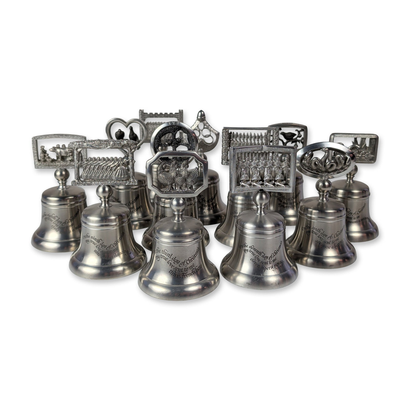 12pc Crown and Rose London Pewter Christmas Bell Set: Crown and Rose, London. Set of twelve cast pewter commemorative handbells themed after The Twelve Days of Christmas. Each bell features a bell-shaped body with an engraved verse from the carol and a c
