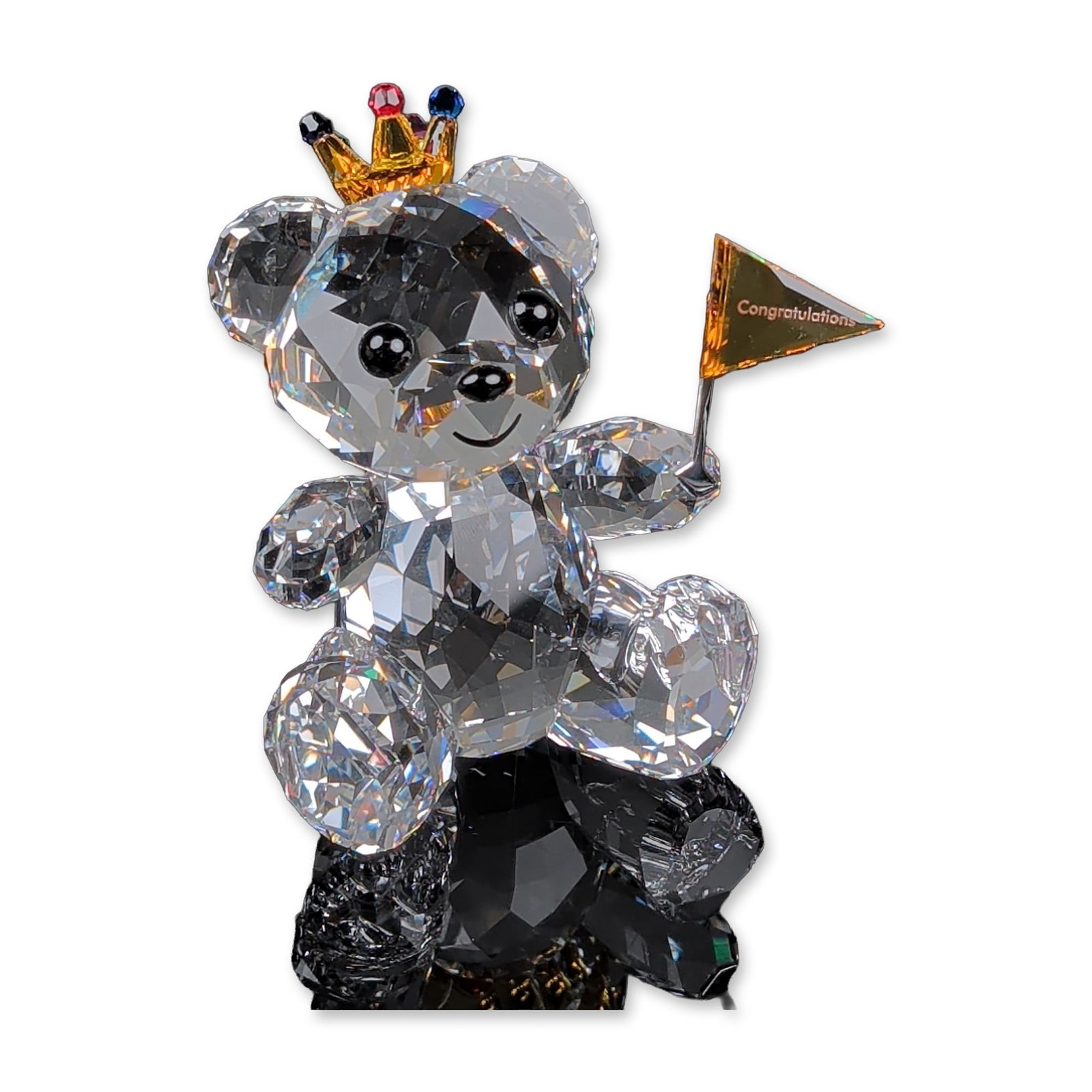 Swarovski Crystal Figurine, Kris Bear Congratulations: The faceted clear crystal bear features black crystal eyes and a printed smile. It wears a gold-toned crown accented with red, blue, green, and pink crystal chatons. The figure holds a gold-toned meta