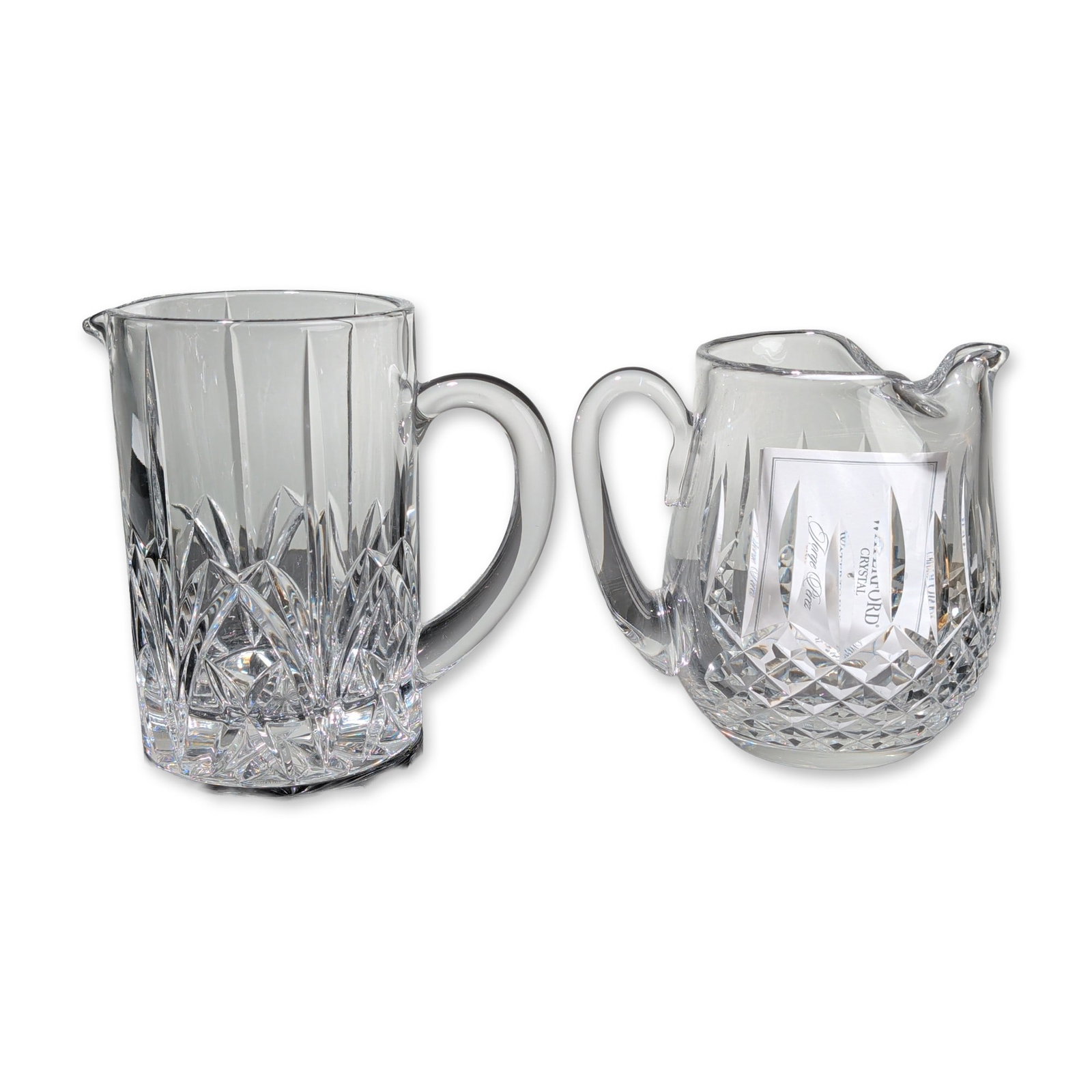 Two Waterford Cut Crystal Pitchers: Clear cut crystal pitchers the first pitcher features a cylindrical form with an ice lip, decorated with vertical wedge cuts over a lower register of crisscrossing geometric fan and diamond cuts. The 