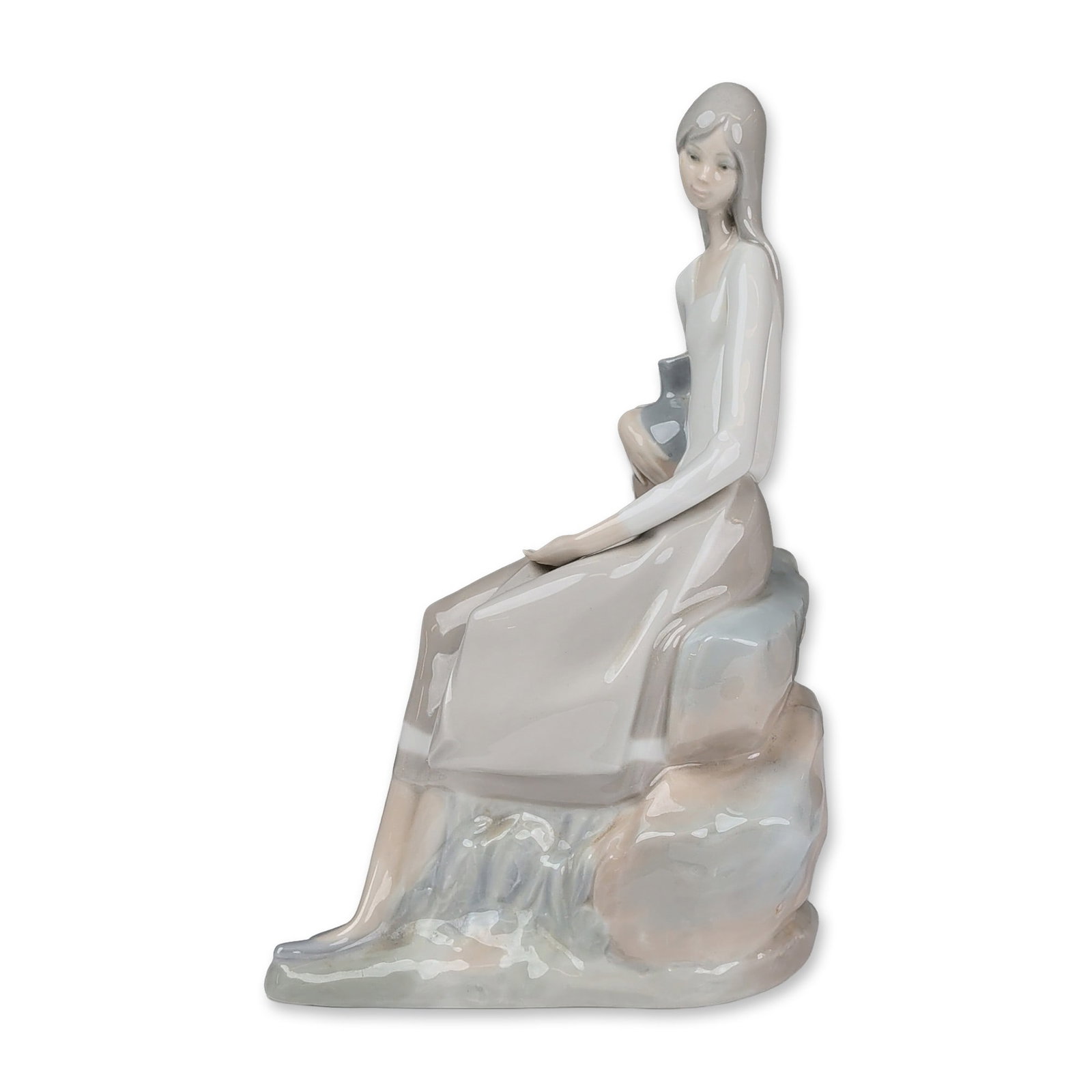 Nao by Lladro Glazed Porcelain Figurine, Woman Sitting on Rock: A glazed porcelain figurine depicting a young woman with long hair seated upon a stylized rock formation in a contemplative pose. The figure displays characteristic elongated proportions and is finish