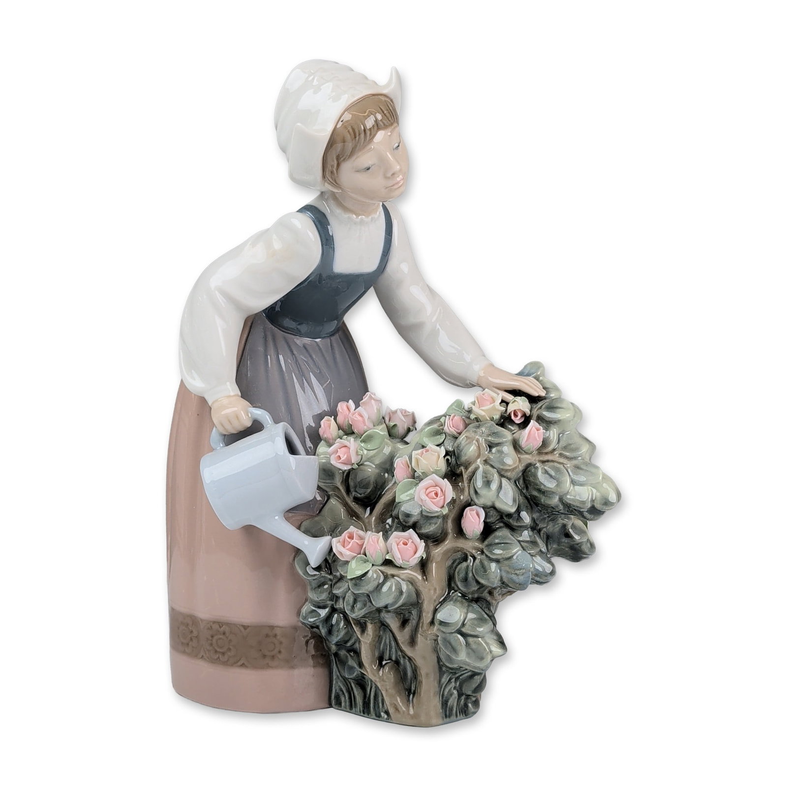 Lladro Porcelain Figurine, Girl Watering 01001354: The figurine depicts a young girl in traditional Dutch dress, featuring a white winged cap, blue bodice with a bow at the back, and a mauve skirt with a patterned floral border. She is posed holding a