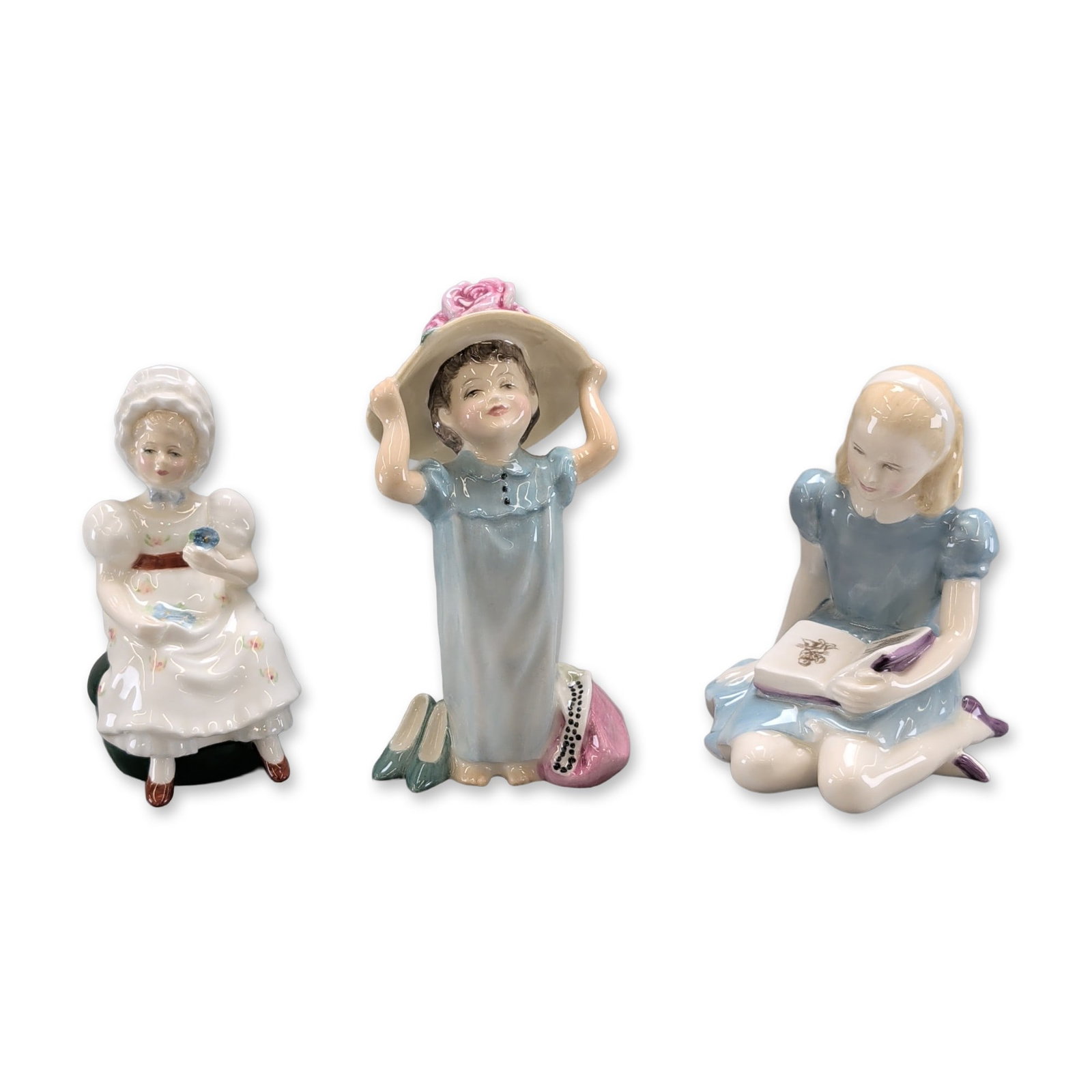 3pc Royal Doulton Figurines, Alice, Kathy, Make Believe: Royal Doulton bone china figurines, England, comprising three hand-painted studies of young girls. The first figure, Alice HN2158, is depicted seated in a blue dress reading a book, featuring a printe