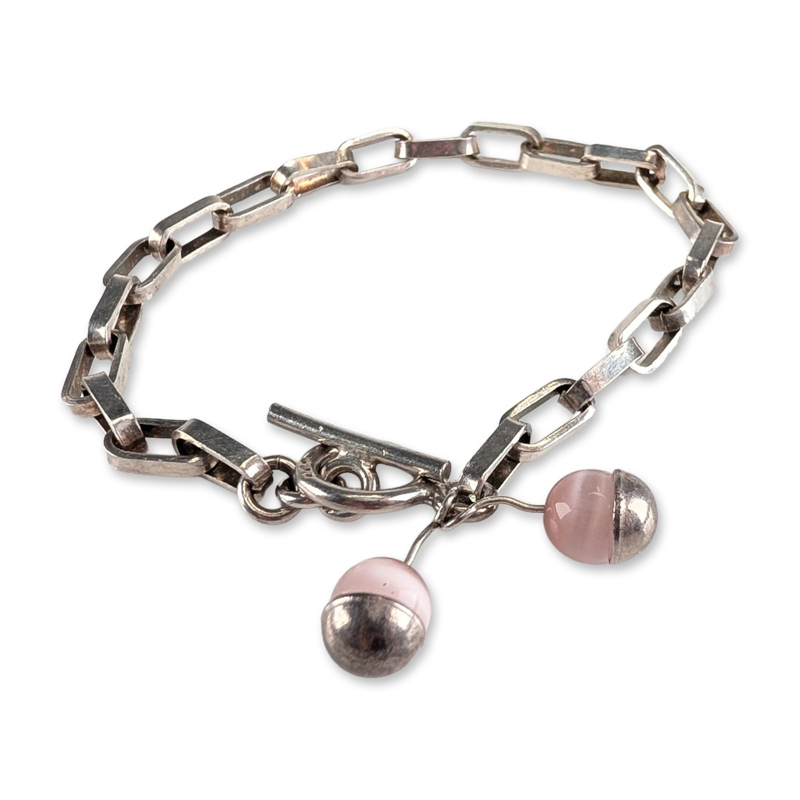 Sterling Silver Pink Cats Eye Bead Link Bracelet: Sterling silver bracelet featuring rectangular bar links and a toggle clasp. The toggle ring serves as a mounting point for two pink chatoyant glass bead drops, each held in a silver hemispherical cap
