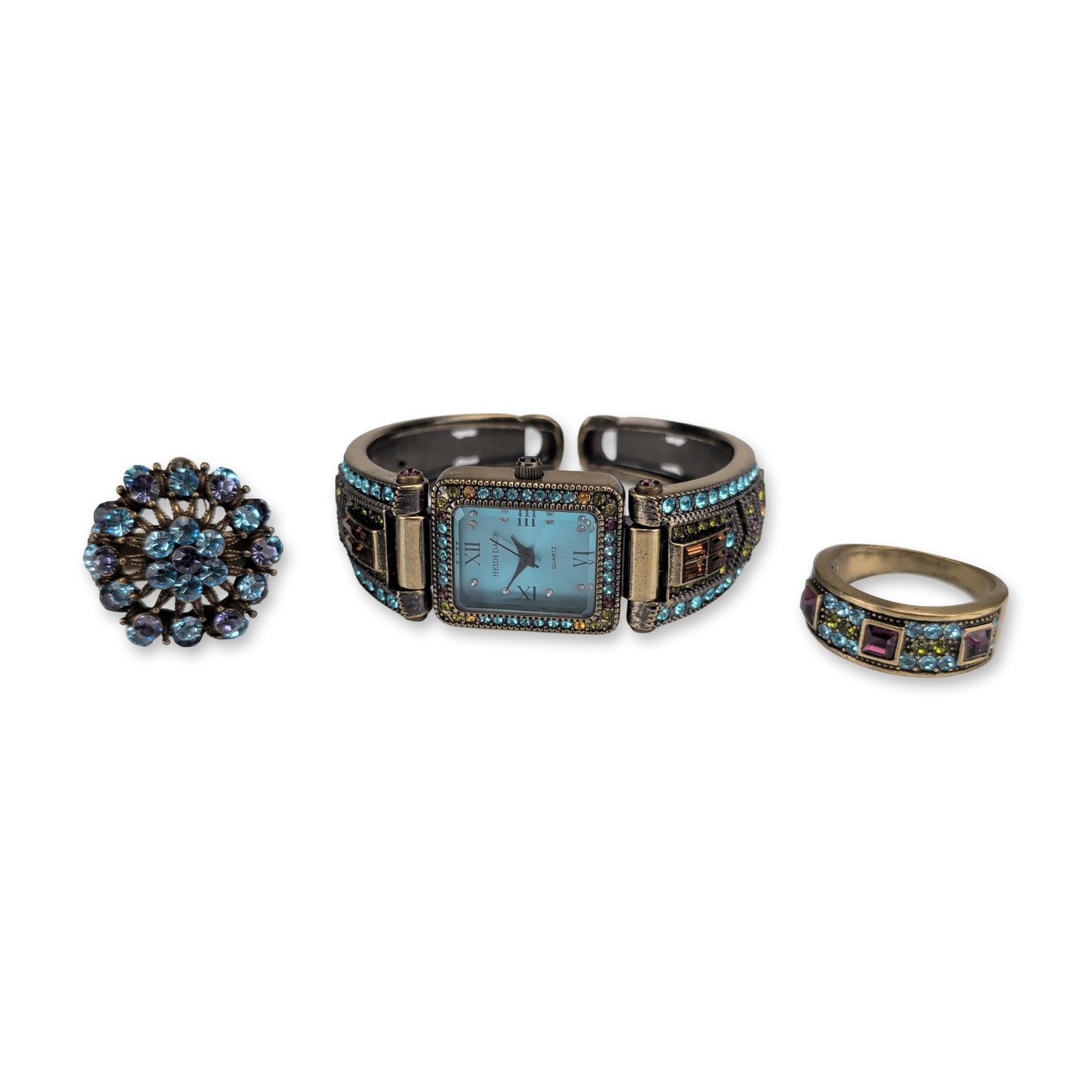 3pc Heidi Daus Bronze Tone Crystal Watch and Rings: Trio of bronze-tone base metal jewelry pieces set with multi-colored faceted crystals in shades of aqua, amethyst, topaz, and peridot. The collection includes a cuff-style watch with a rectangular lig