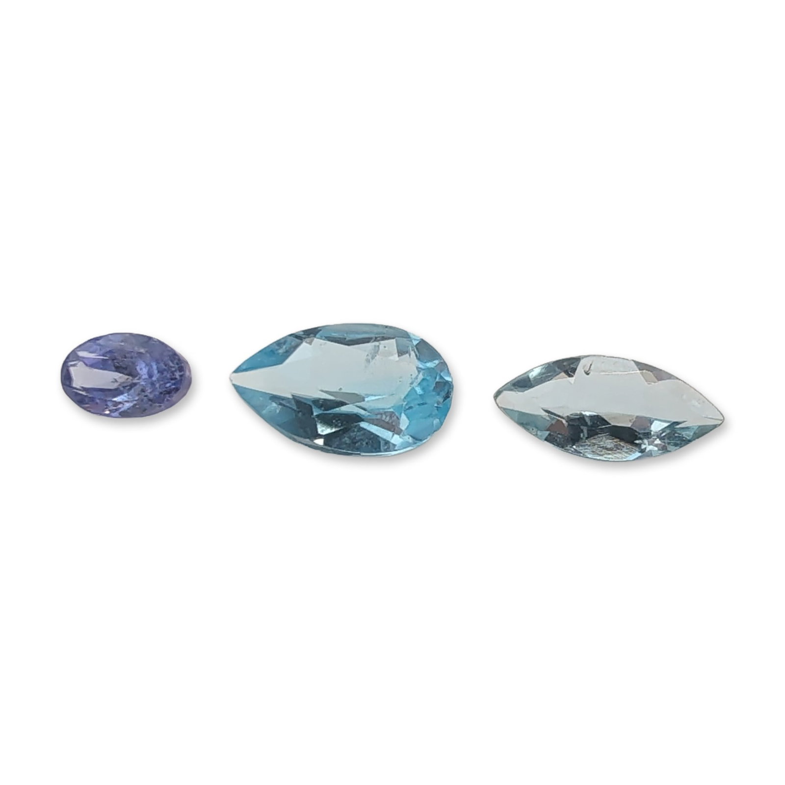 Group of Three Loose Faceted Blue Tanzanite, Topaz, and Citrine Gemstones: Group of three loose faceted gemstones in shades of blue and violet-blue. The grouping includes one oval-cut gemstone with a violet-blue hue, which appears to be tanzanite. Featuring visible internal 