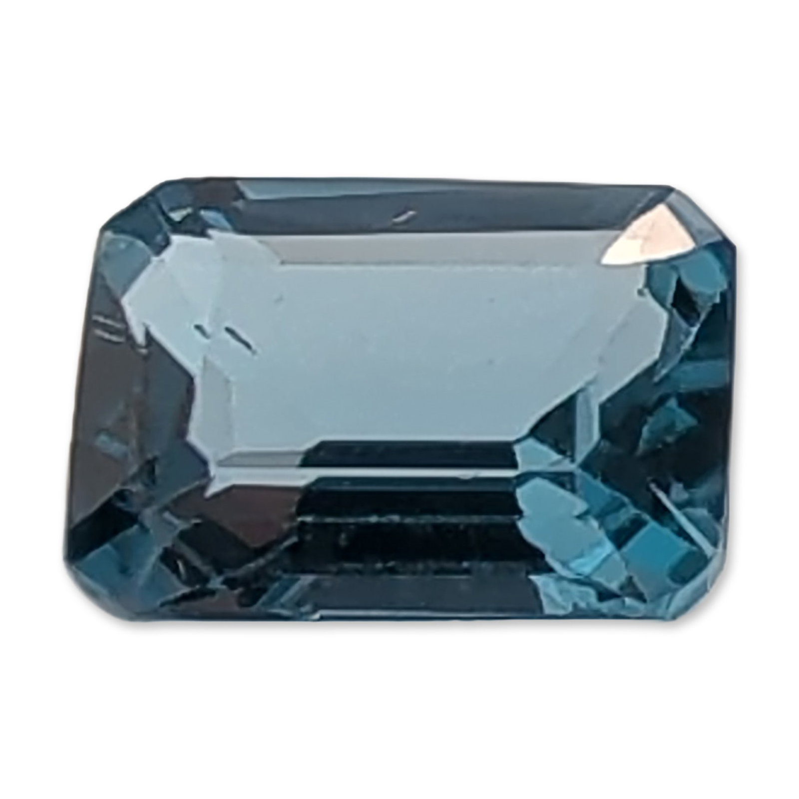 Emerald Cut Blue Topaz Gemstone: Loose rectangular emerald cut Topaz gemstone in a deep teal-blue color. The stone features truncated corners and step-cut facets with a well-proportioned pavilion. Accompanied by a hand-written tag no