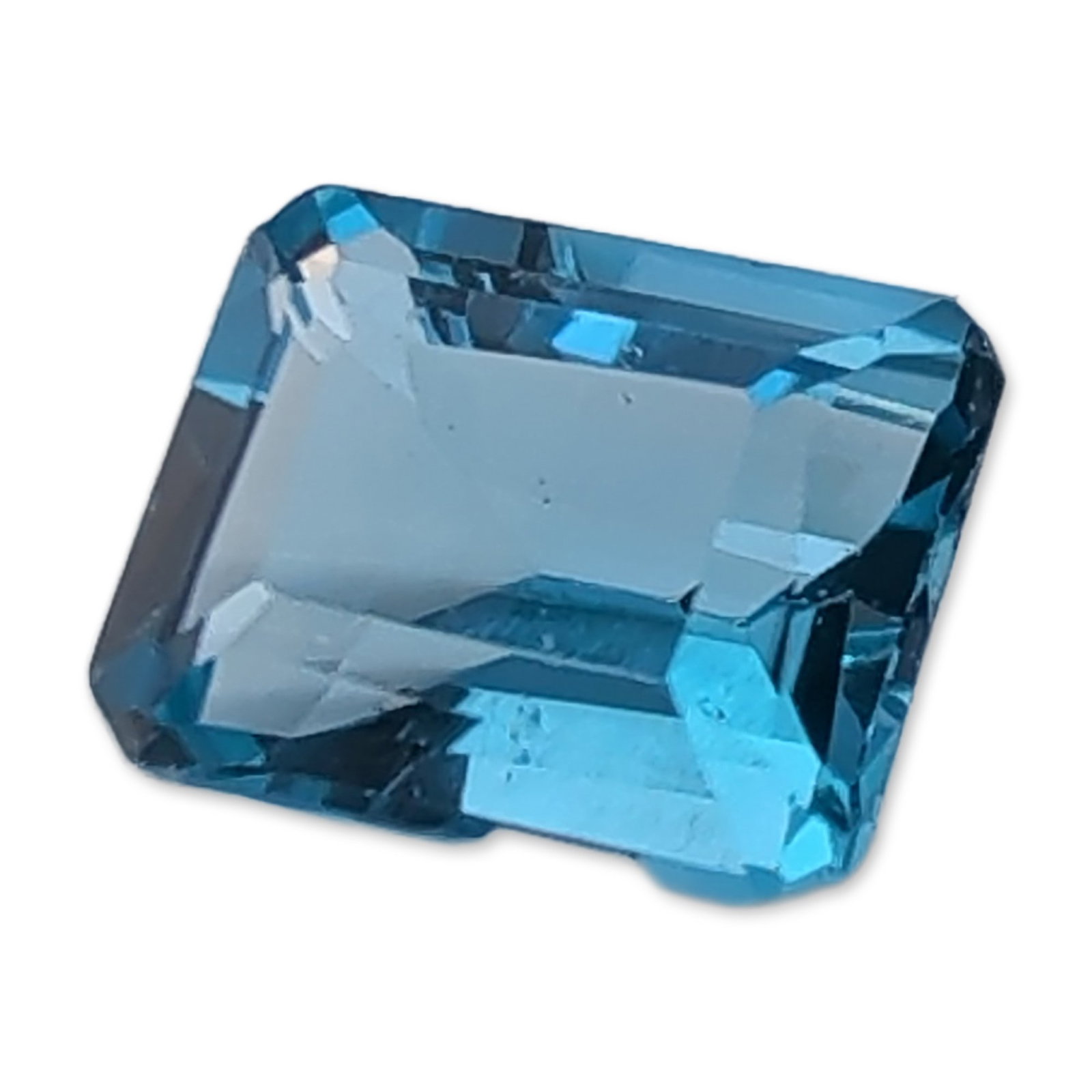 Loose Emerald Cut Swiss Blue Topaz: Loose faceted Swiss blue topaz. The stone features a rectangular emerald cut with step facets and clipped corners, exhibiting a vibrant medium blue color and good clarity. No formal laboratory certifi
