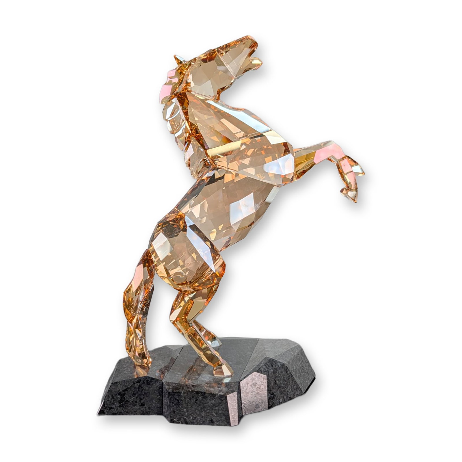 Swarovski Stallion Golden Shine Crystal Sculpture: Swarovski Stallion Golden Shine sculpture in faceted golden shadow crystal, depicting a rearing horse in a dynamic pose. The figure is mounted on a multi-faceted dark grey stone base. Designed by Hein