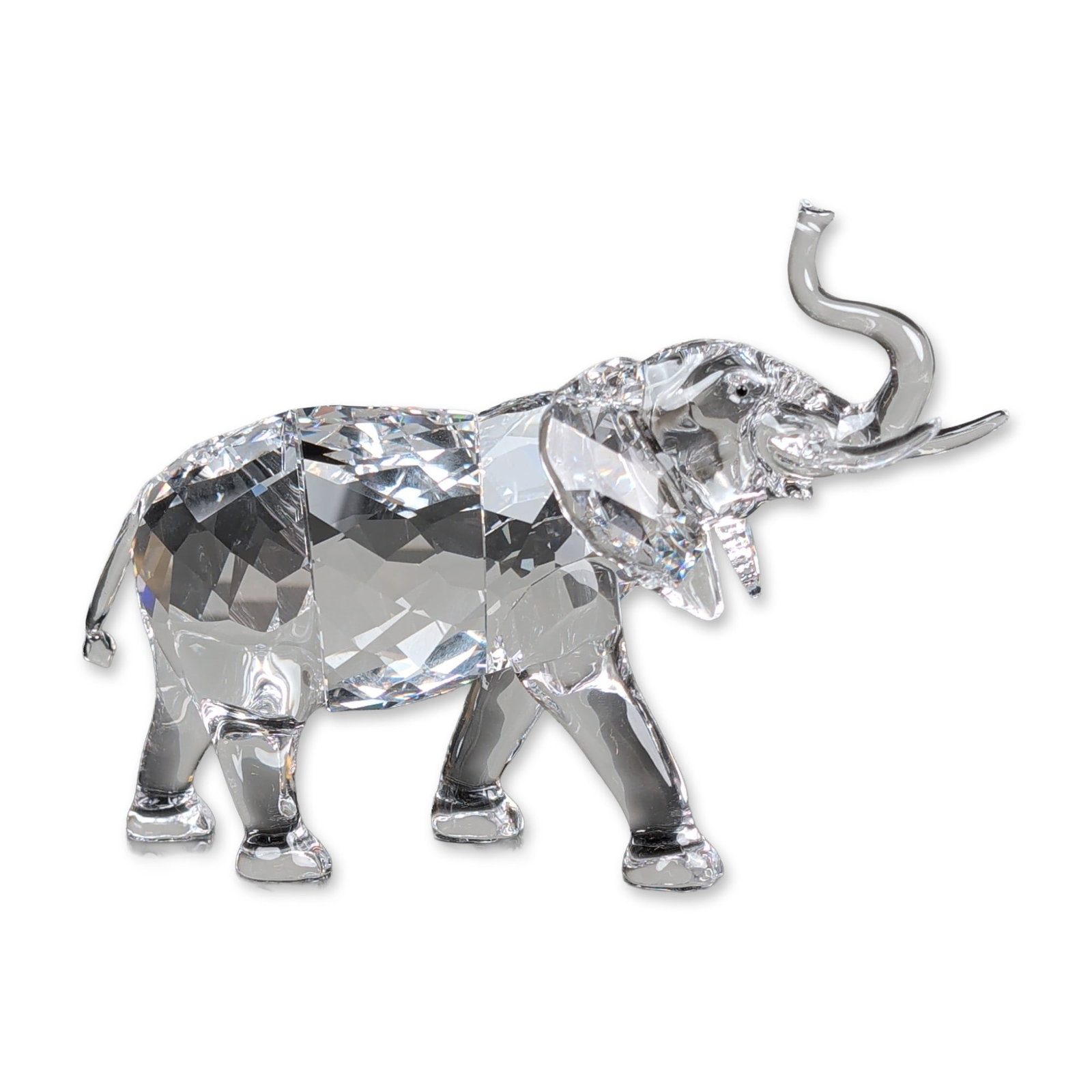 Swarovski Crystal Elephant Figurine from Rare Encounters Series: Swarovski Elephant figurine in clear faceted lead crystal, featuring a smooth-polished crystal head, trunk, and legs. Designed by Heinz Tabertshofer, the elephant is depicted with a raised trunk and i