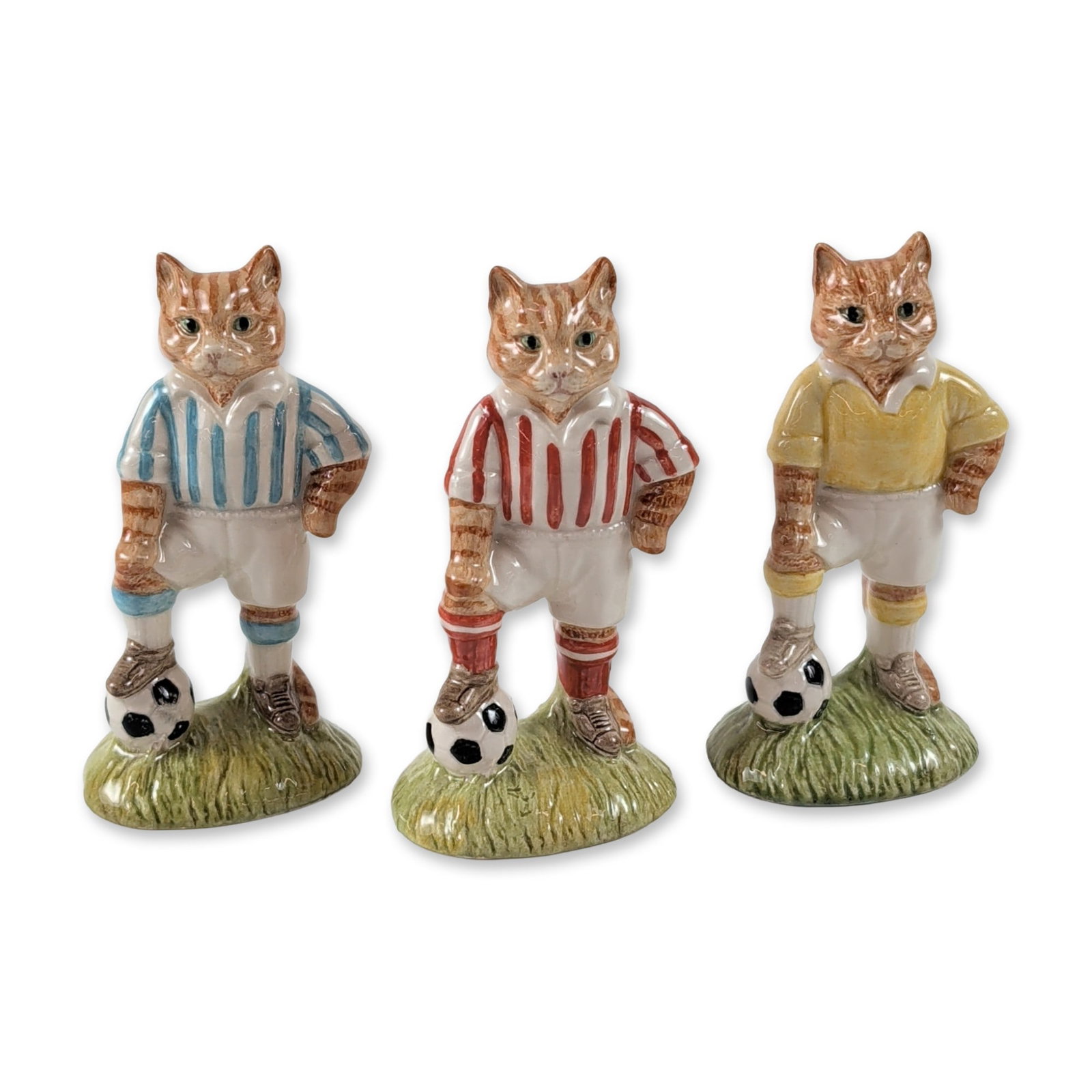 3pc John Beswick Sporting Cats: John Beswick (English, 1987). Three ceramic figurines from the Sporting Cats series, depicting ginger tabby cats as soccer players. Each cat is modeled standing on a textured green grass base with one