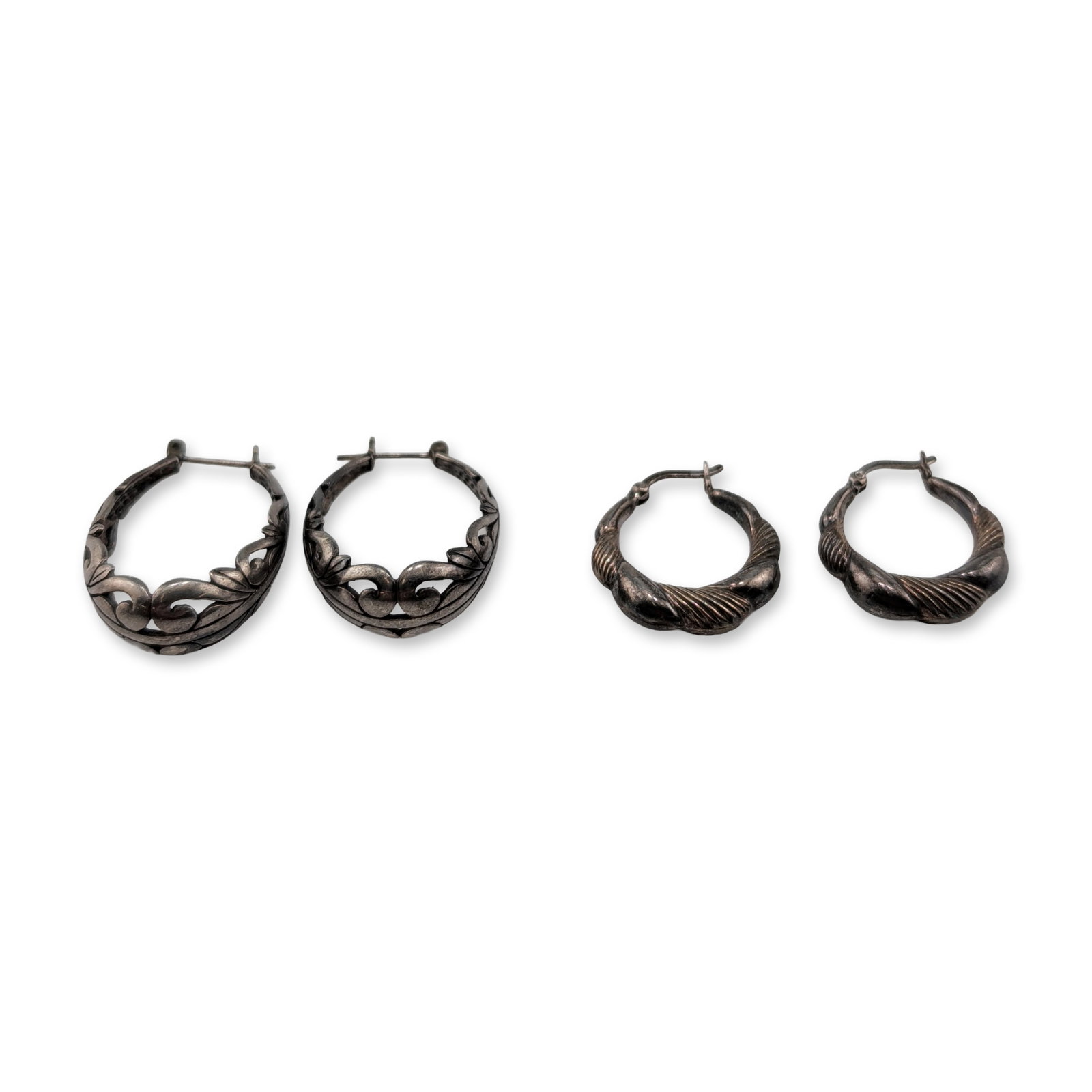 Two Pairs of Sterling Silver Hoop Earrings: Two matched pairs of sterling silver hoop earrings. The first pair features a tapered design with diagonal ribbed texture, secured with hinged wire lever back closures and stamped 925 on the wire.