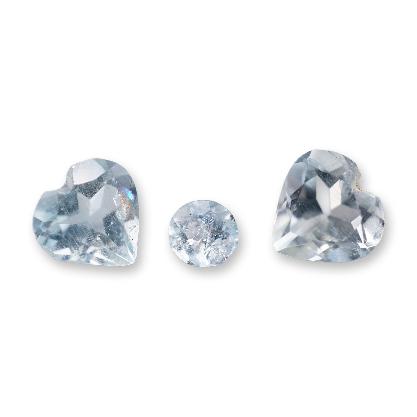 Trio of Loose Aquamarine Gemstones: Trio of loose faceted aquamarine gemstones, including two matching heart-shaped stones and one round brilliant-cut stone. The stones feature a pale watery blue color with visible internal veining and
